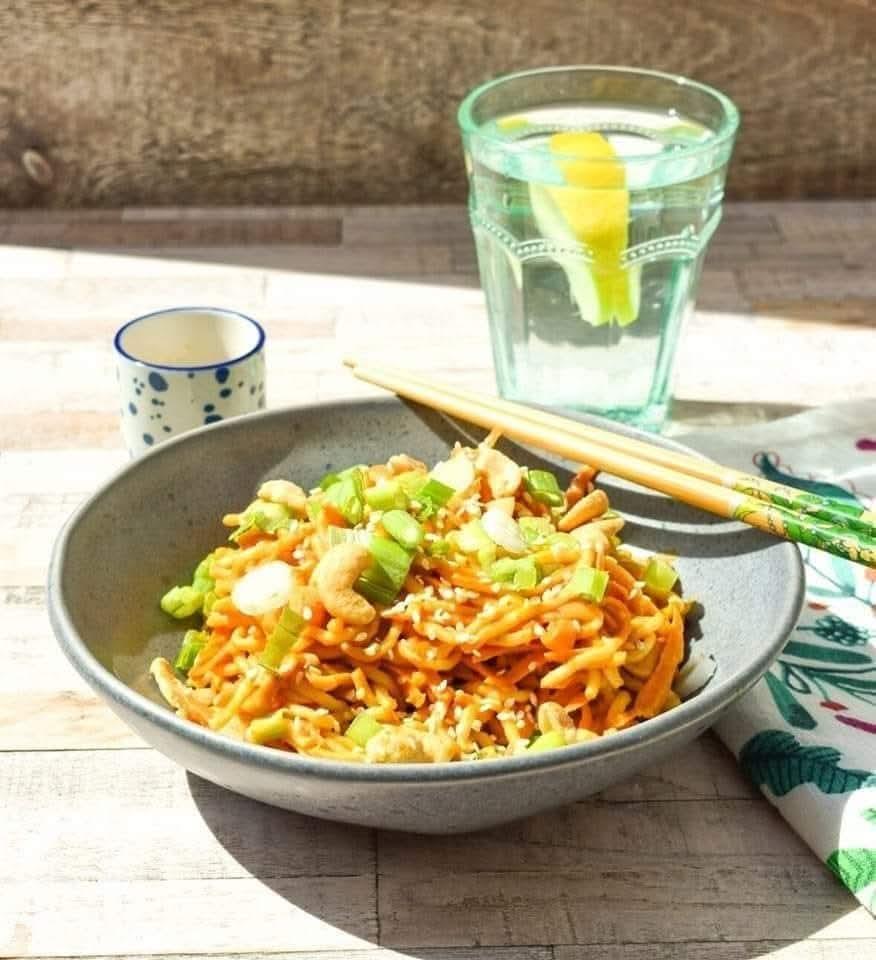 Bowl of noodles topped with spring onion and sesame seeds.