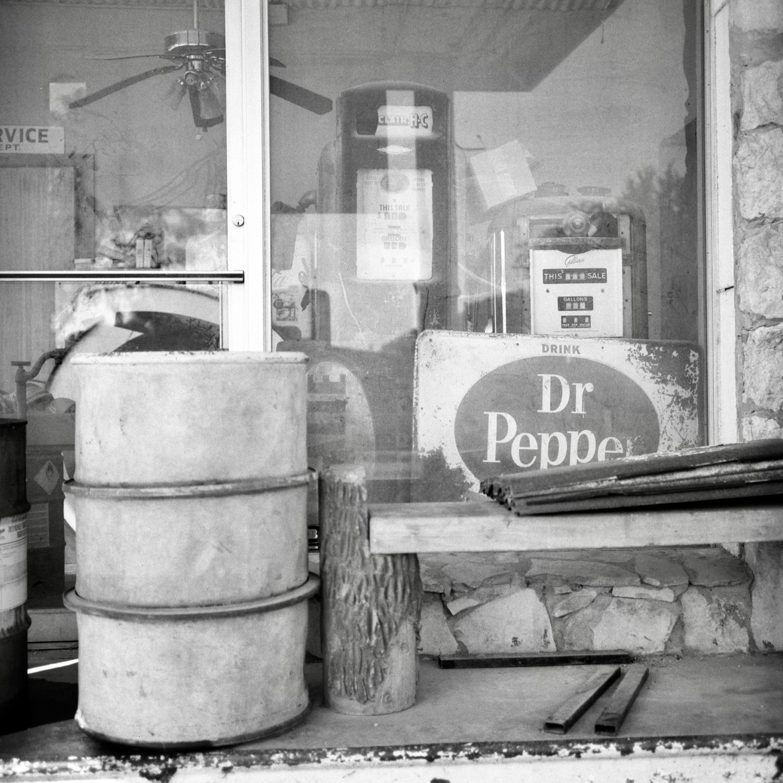 A black-and-white film photo. Two very old gas pumps and a weatherworn Dr Pepper sign are seen through the front window of an abandoned service station in Bandera, Texas. Sunday, August 2, 2026.
