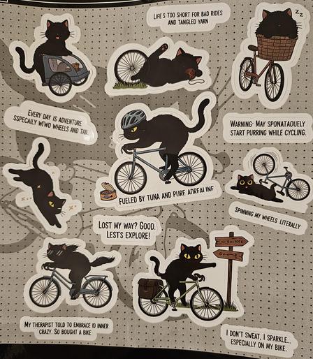 Cartoon stickers featuring cats and bicycles, some of which have badly written captions like "Lost my way? Good. Lests Explore!" or "My therapist told me to embrace IO inner crazy. So bought a bike"