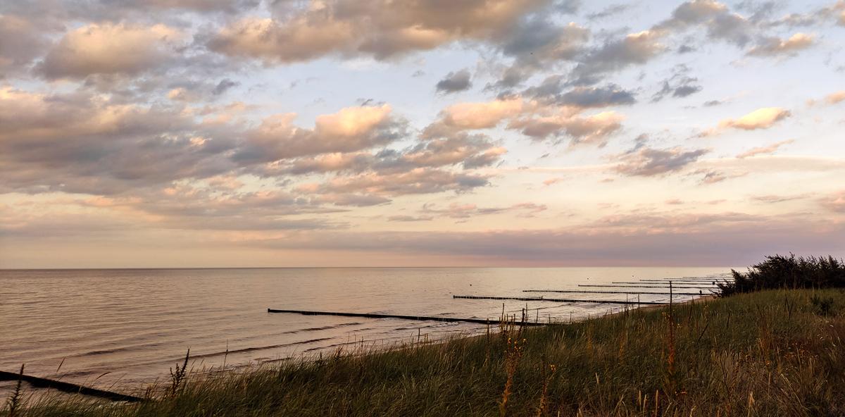 Ostsee Foto Sonnenuntergang. Diagonale Aufteilung, Links-oben Meer mit Bunen; rechts-unten wilde Dünenwiese.