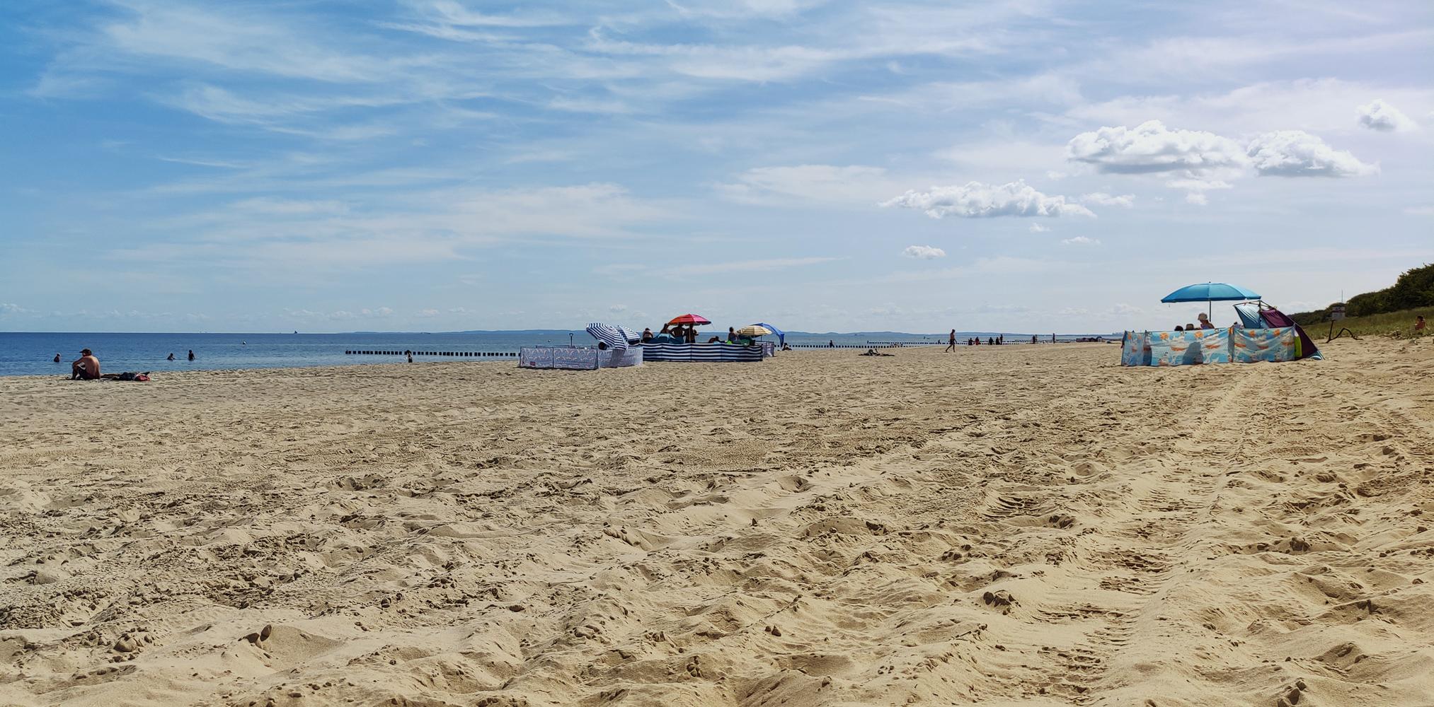 Ostseeklassiker. Untere Hälfte mit sehr viel Sand. Obere Hälfte Himmel mit dramatischem Wölkchen, Meer und vereinzelte Strandburgen (Windschutzbauten) auf der Trennlinie