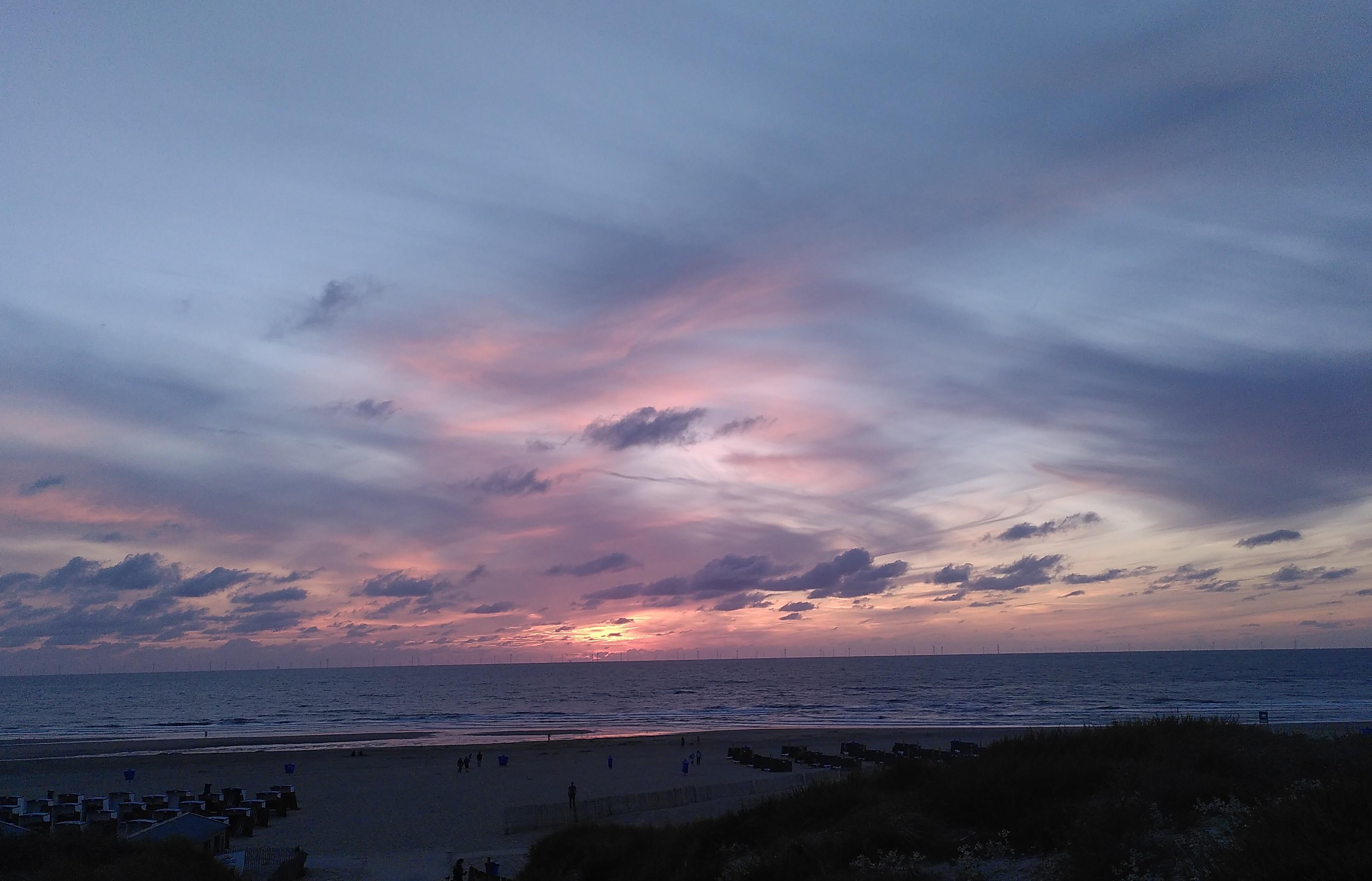 Criss-crossed clouds after sunset in blue, white and pink above open water.