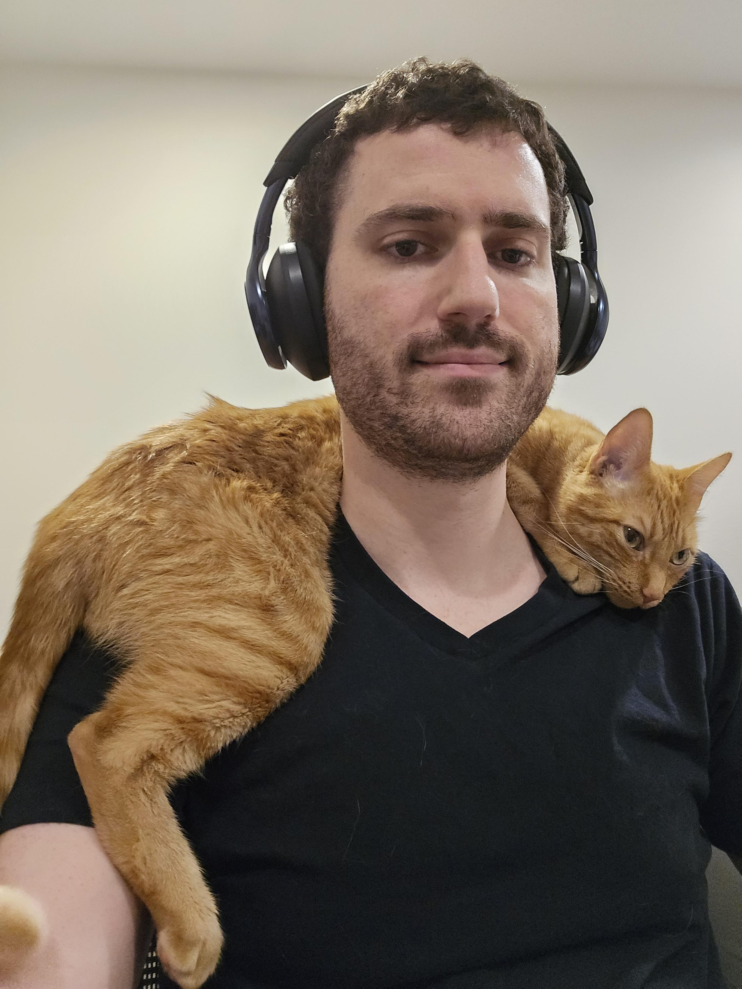 A selfie of a person with an orange tabby cat draped over their shoulders