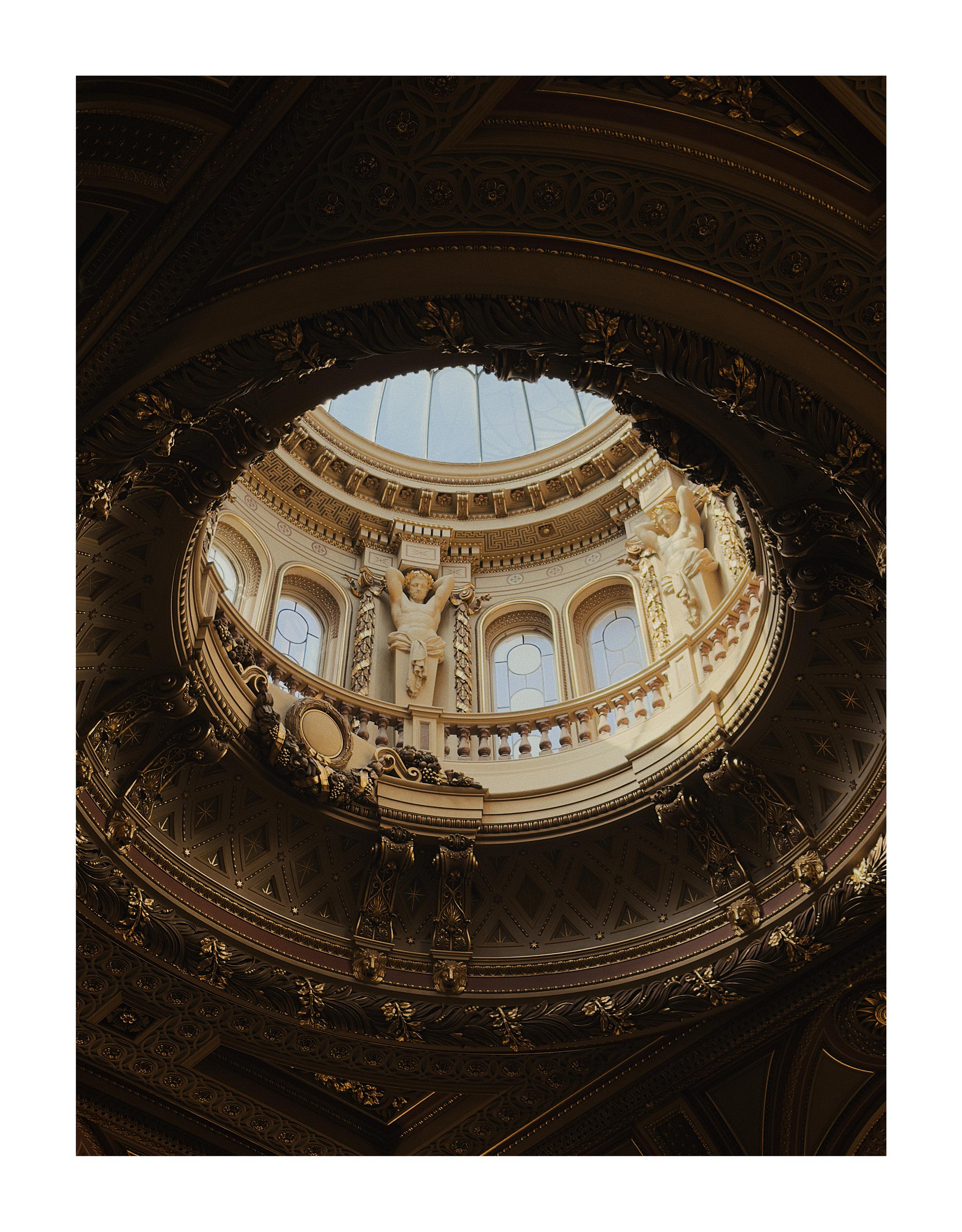 Looking up at a glass dome in a golden coloured, ornate ceiling.