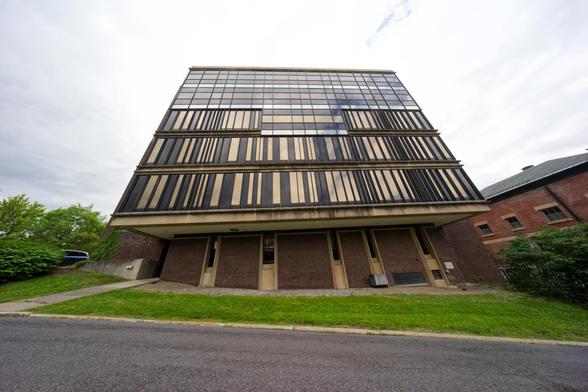Buildint with windows that form dark brown and yellow bars on the other floors turning to a reflective grid near the top with a road in front