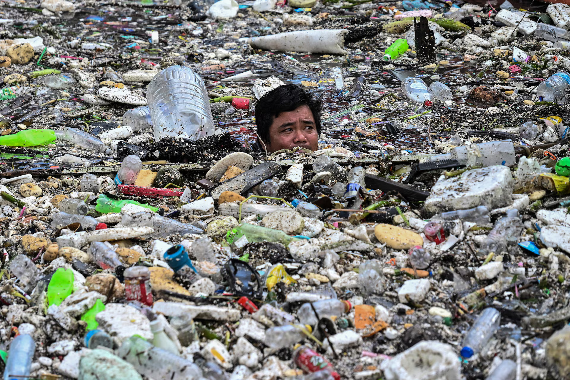 A worker up to his neck in water, collects garbage that washed into a river.