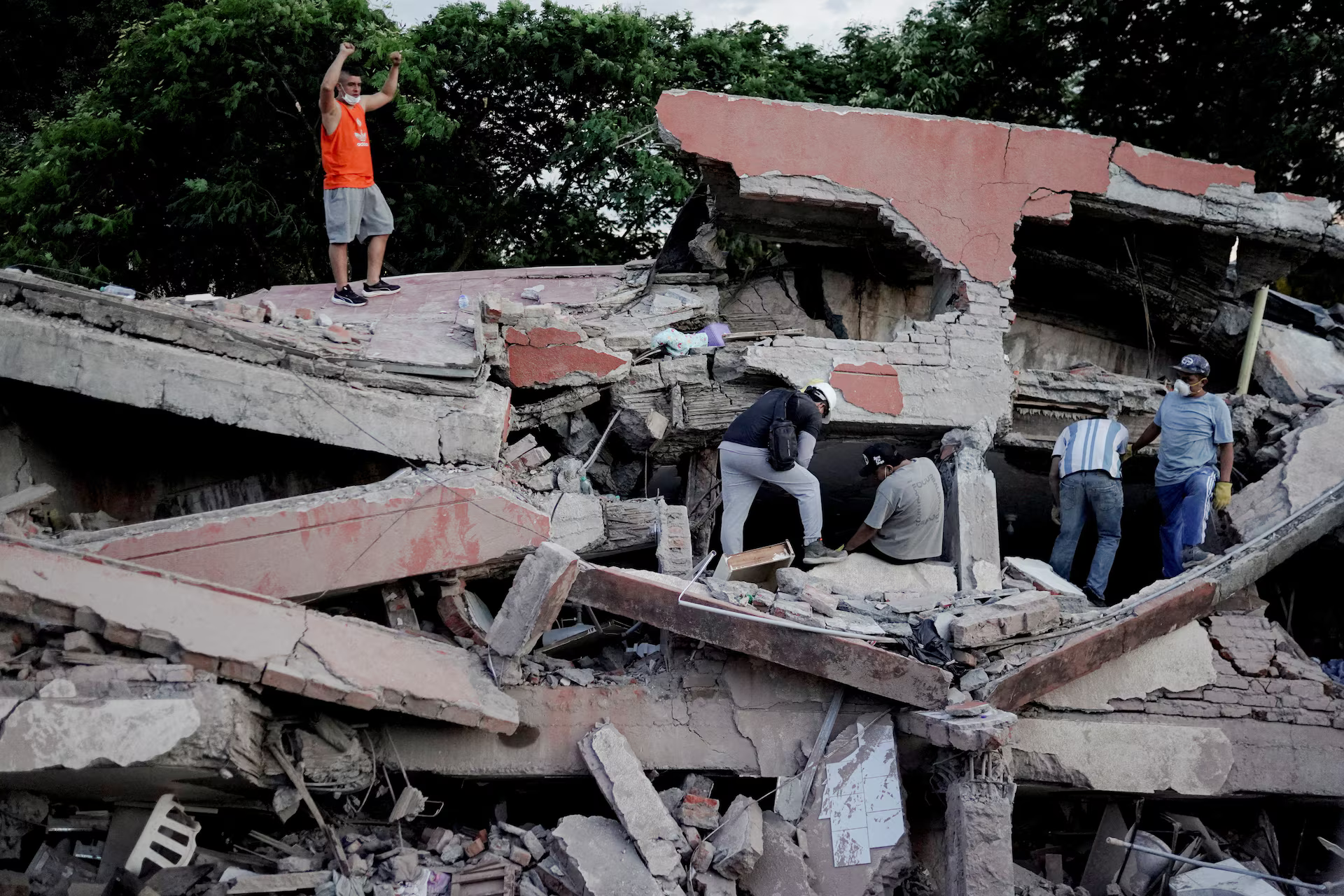A rescue worker raises his fists to call for silence to locate victims under the rubble at the site of a collapsed building.