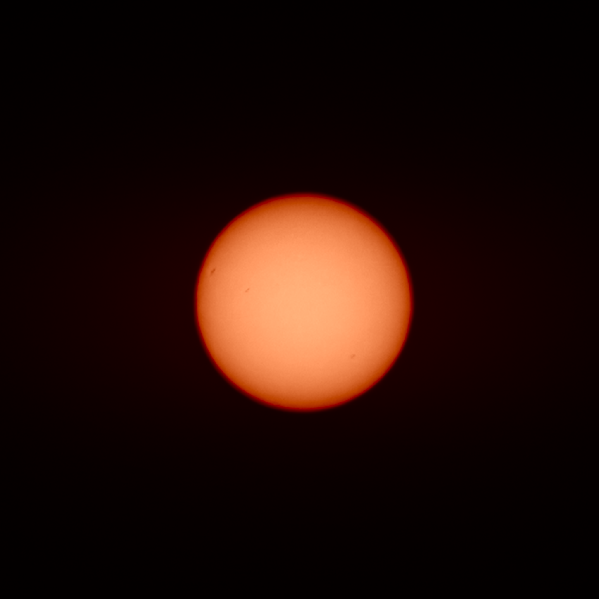 An image of the Sun seen through a zoom lens on a mirrorless camera, showing a few sunspots. The image was converted to monochrome then colourised to show a yellow middle and a redder limb.