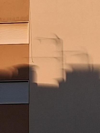 Weirdly distorted shadow of the top of a building, still with some tv antennas, cast onto the wall of another.