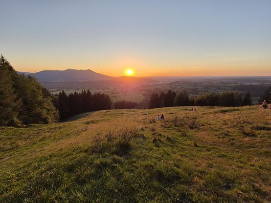 A mountainous landscape with the sun setting in the distance