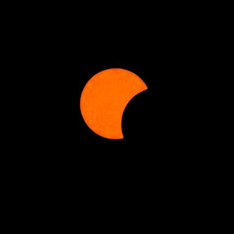 Mit hohem Kontrast die Sonne partiell vom Mond bedeckt. Die Sonne als Kreis in kräftigem Orange durch den Schutzfilter, rechts unten rund abgeschnitten schiebt sich der Mond vor die Sonne. Der Hintergrund rabenschwarz durch die dunkle Einstellung.