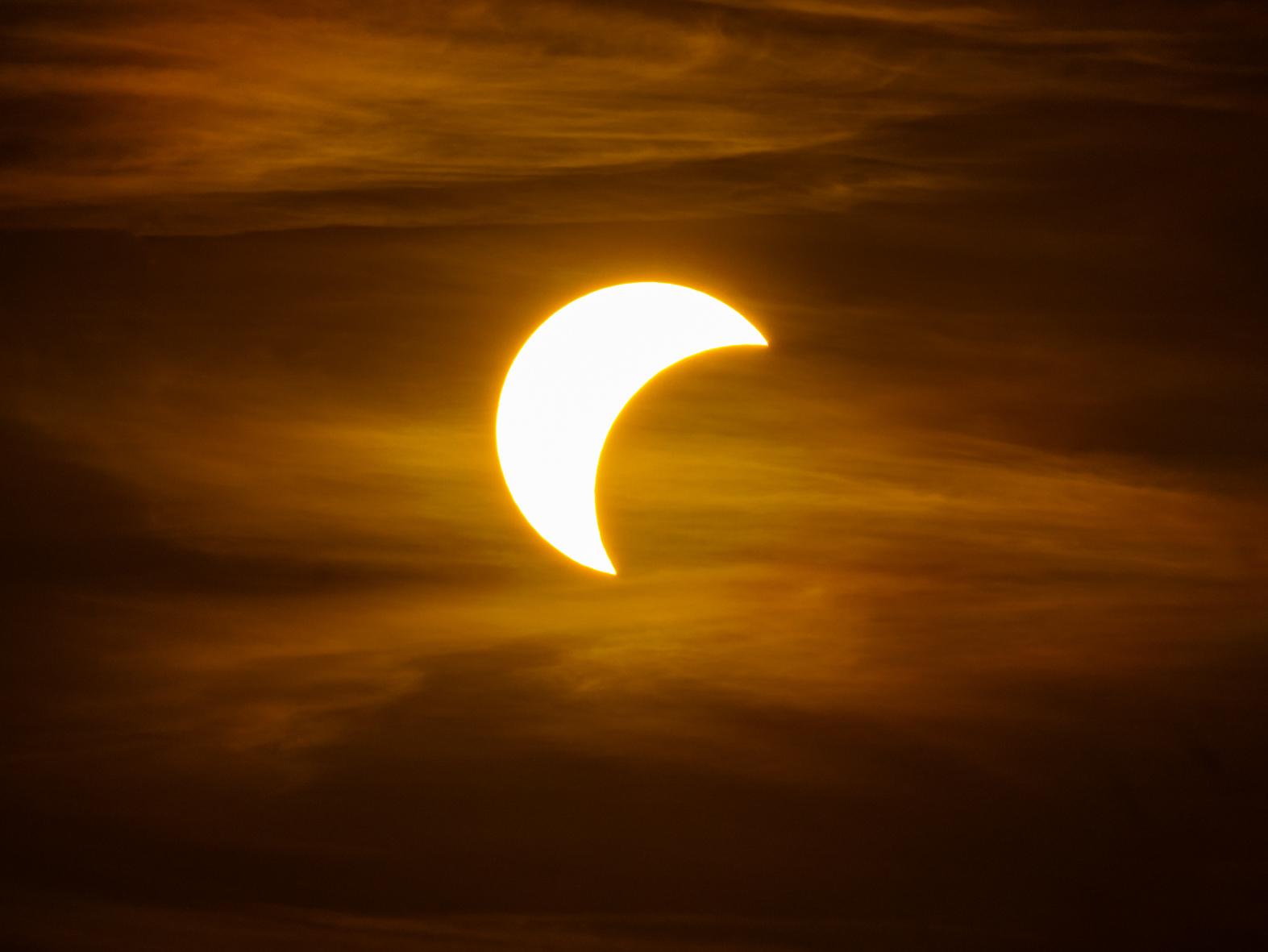 Ein oranger leicht bewölkter Himme, im Zentrum die helle Sonnenscheibe, von der auf der rechten Seite etwa die Hälfte fehlt.