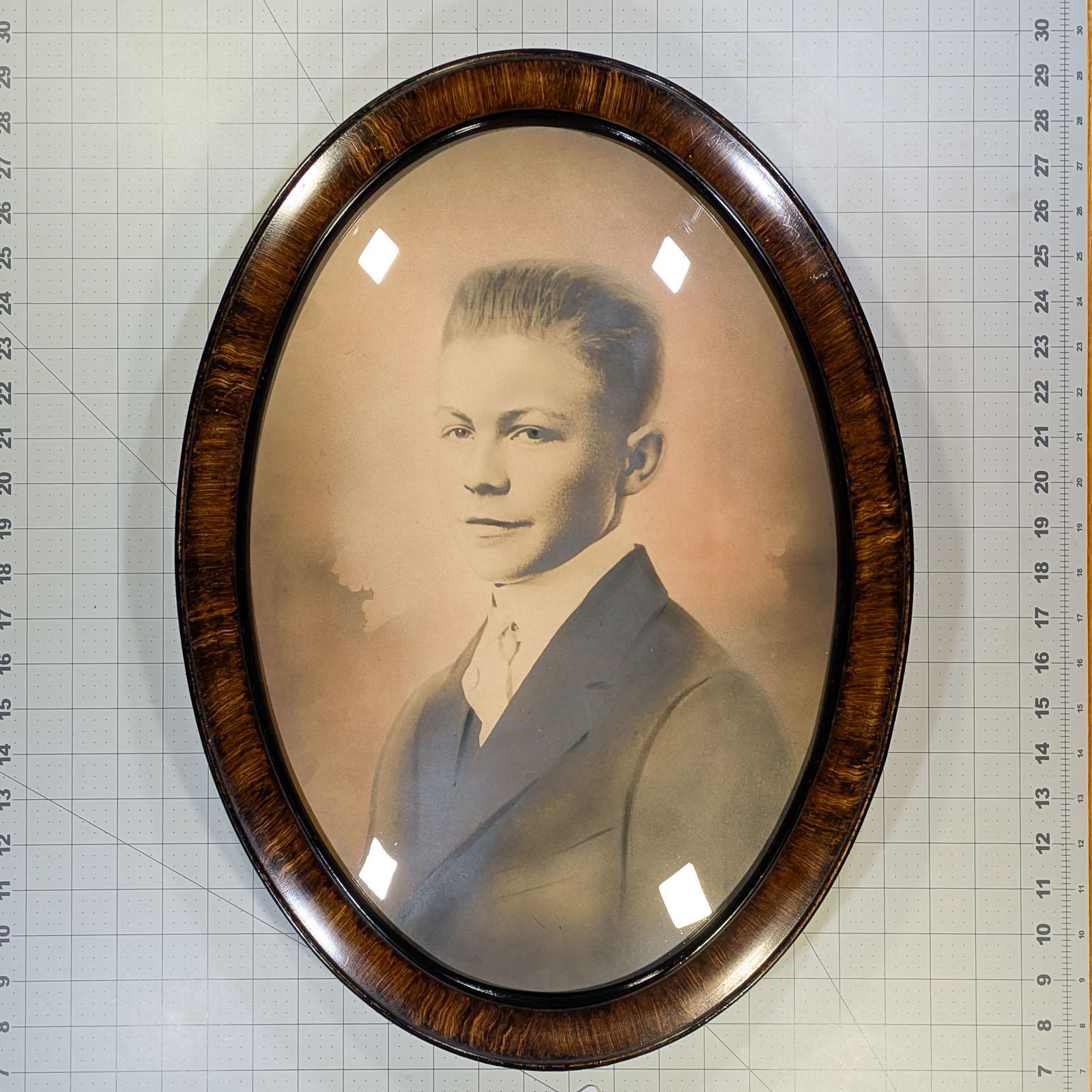 An antique sepia colored photograph of a teenager in a bubble glass frame with a simulated tiger wood edge