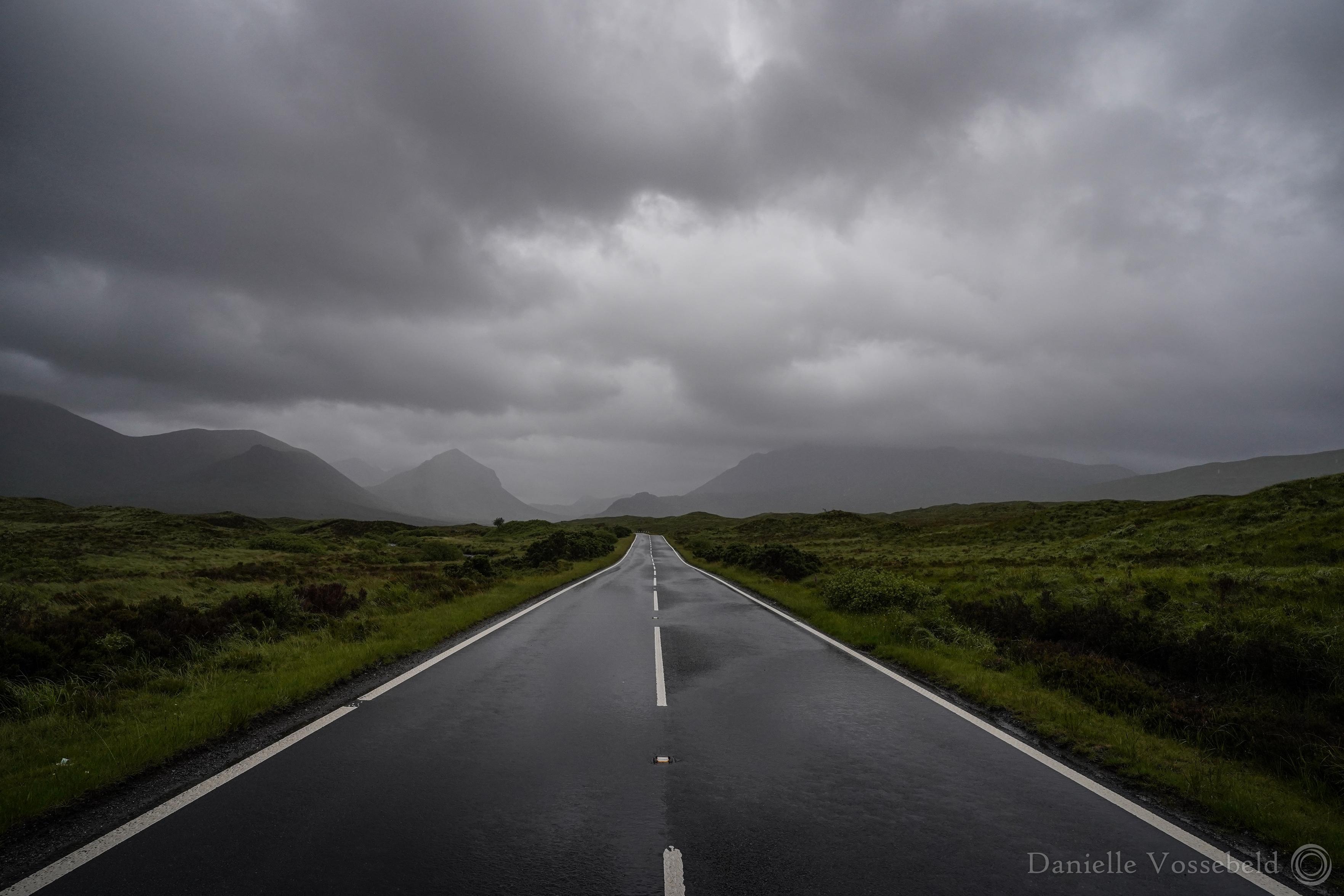 Moody atmosphere. A wet road , grey clouds, dark green sides to the road. In the distance there are mountains. That’s it. Just beautiful.