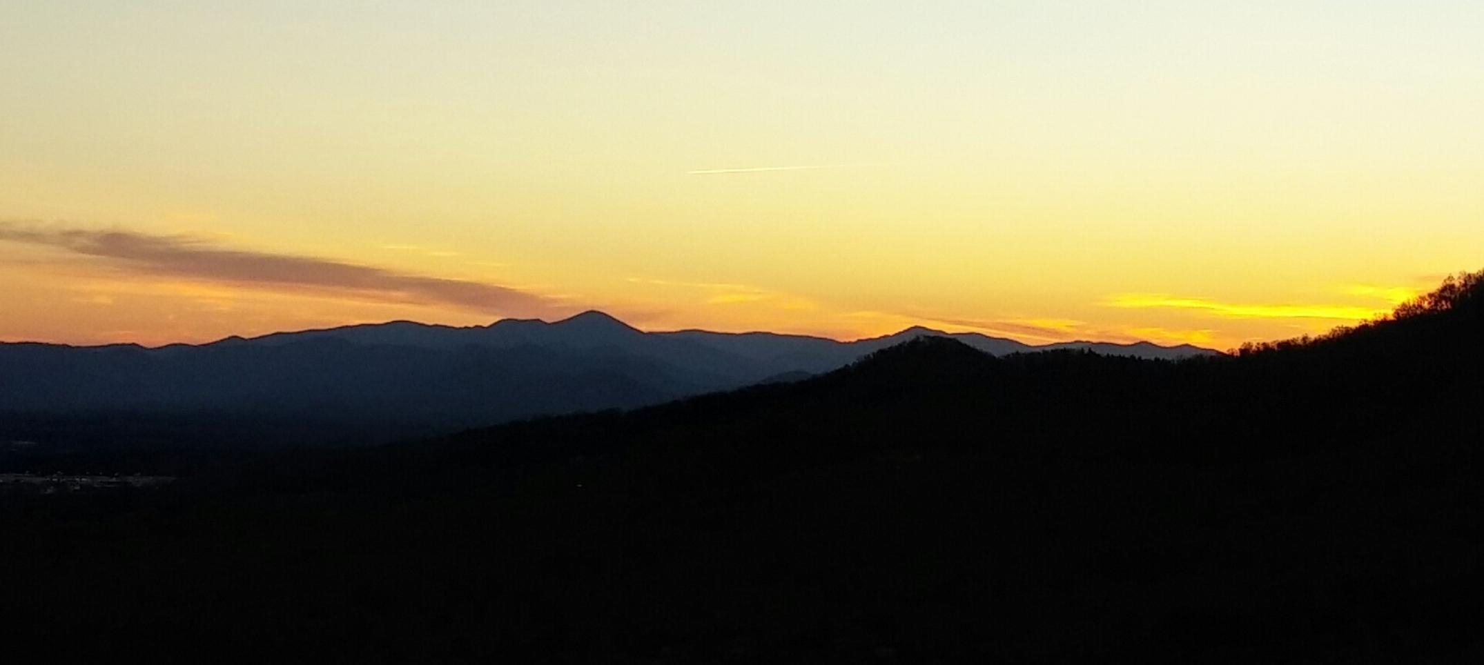 Bright  yellow sunset skies above dark mountains with wispy clouds