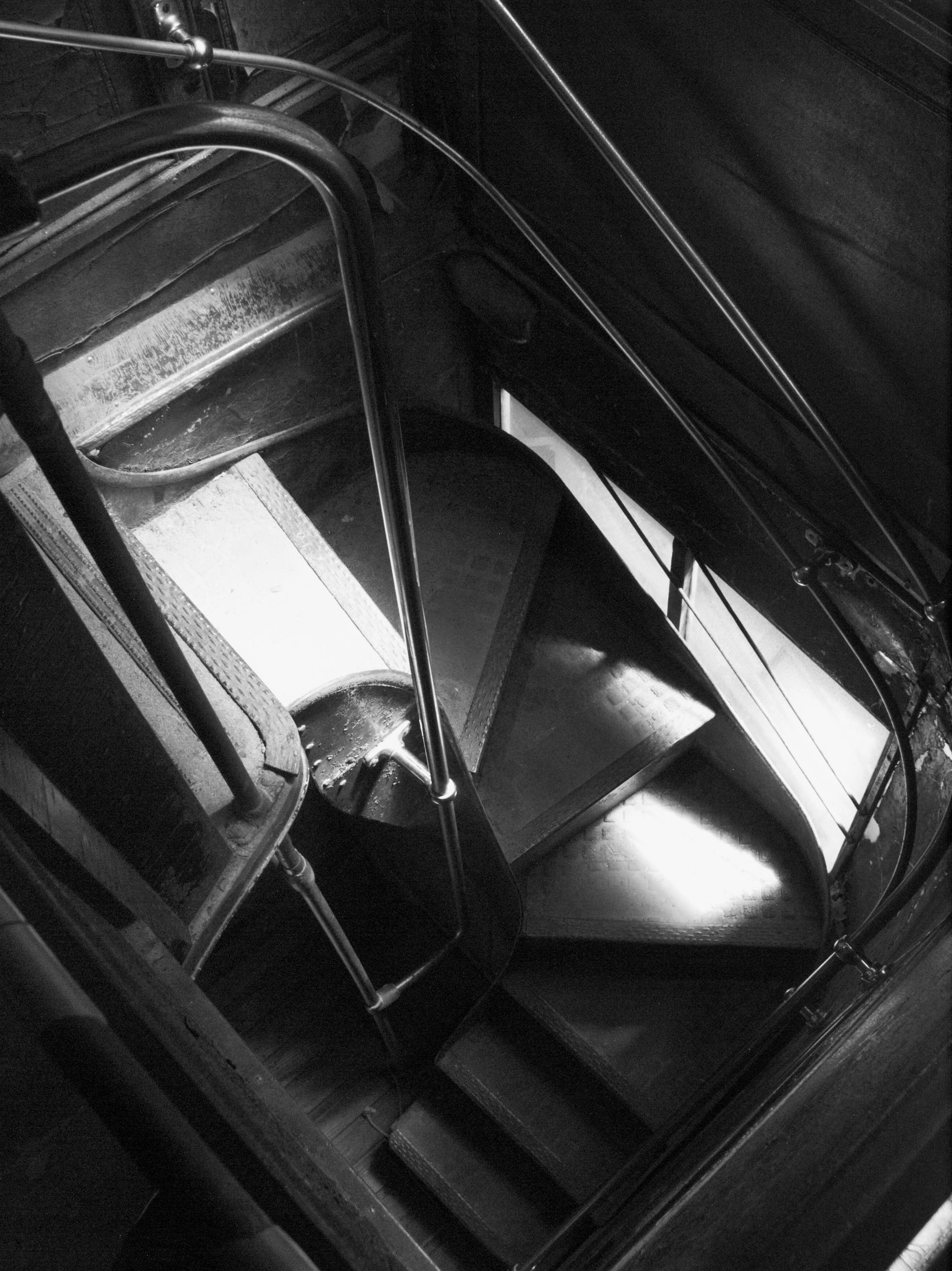 Stairs winding down from the top level of an abandoned double decker trolley. Light filters through the windows.