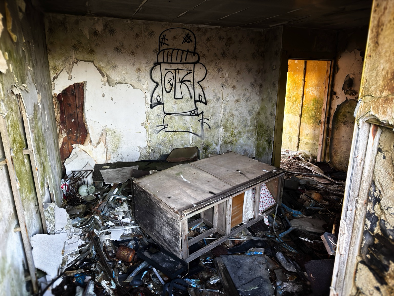 This image shows the inside of the ruined Croft. There is a table in the middle of the floss base. The walls are a dawned with graffiti and it shows a general rundown of the building.