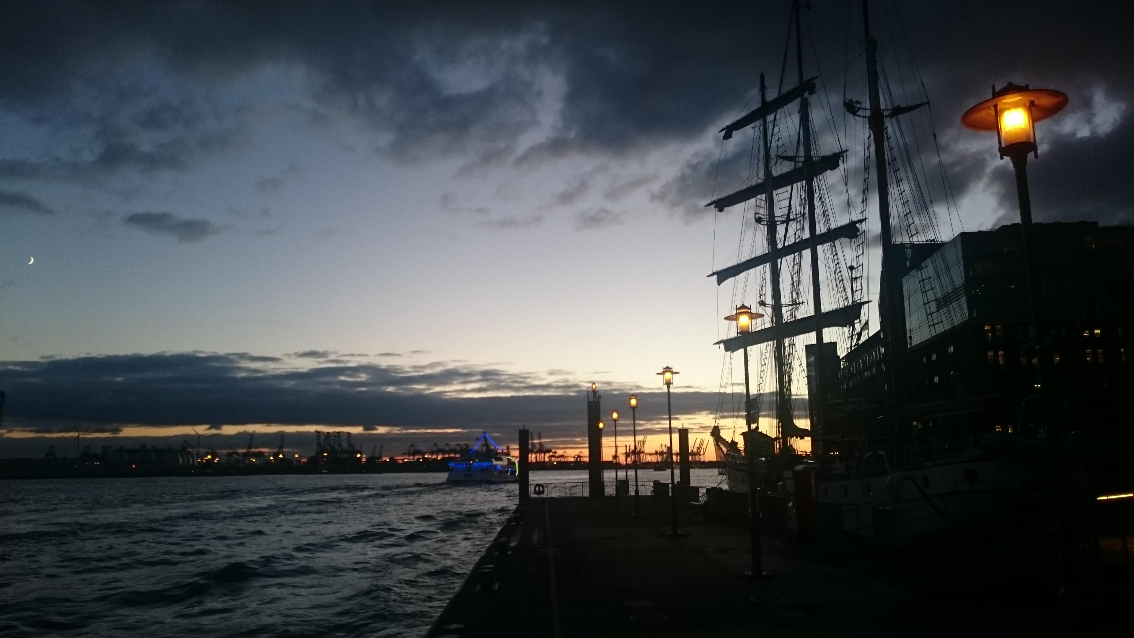 Hamburger Hafen. Letze Nachtdämmerung. Zwei niederländische Segelschiffe ankern. Die Tolkien und die Loth Lorien. Eine Hafenlampe leuchtet gelb. Der Halbmond ist zu sehen.
