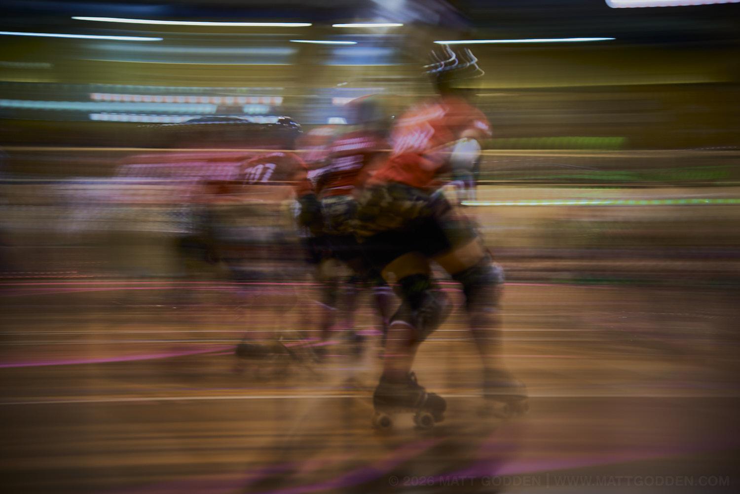 A long exposure image of roller derby competitors from the D'Viants (lime green)Beauty School Knockouts (pink), and the Screaming Assault Sirens (red). 2013/11/09
