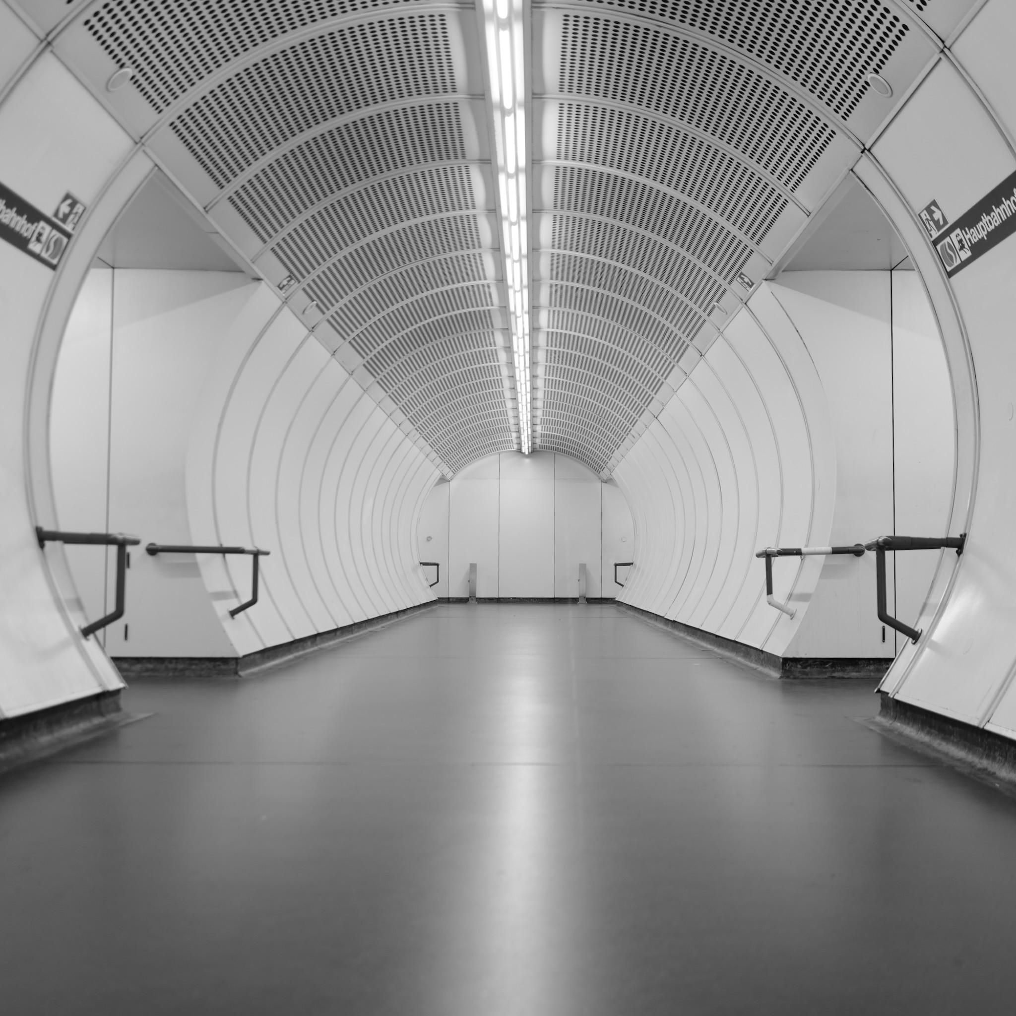 Picture shows an empty floor in a subway station in Vienna. No human visible. Shaped like a round tube. Picture is bright and white is dominant color. Floor is dark.