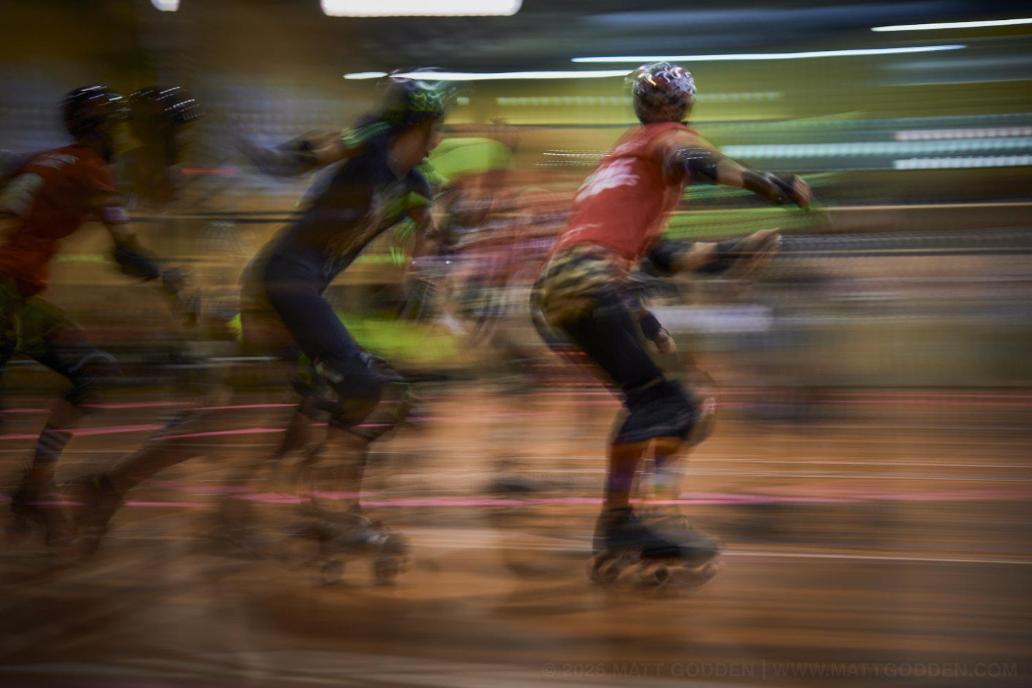 A long exposure image of roller derby competitors from the D'Viants (lime green)Beauty School Knockouts (pink), and the Screaming Assault Sirens (red). 2013/11/09