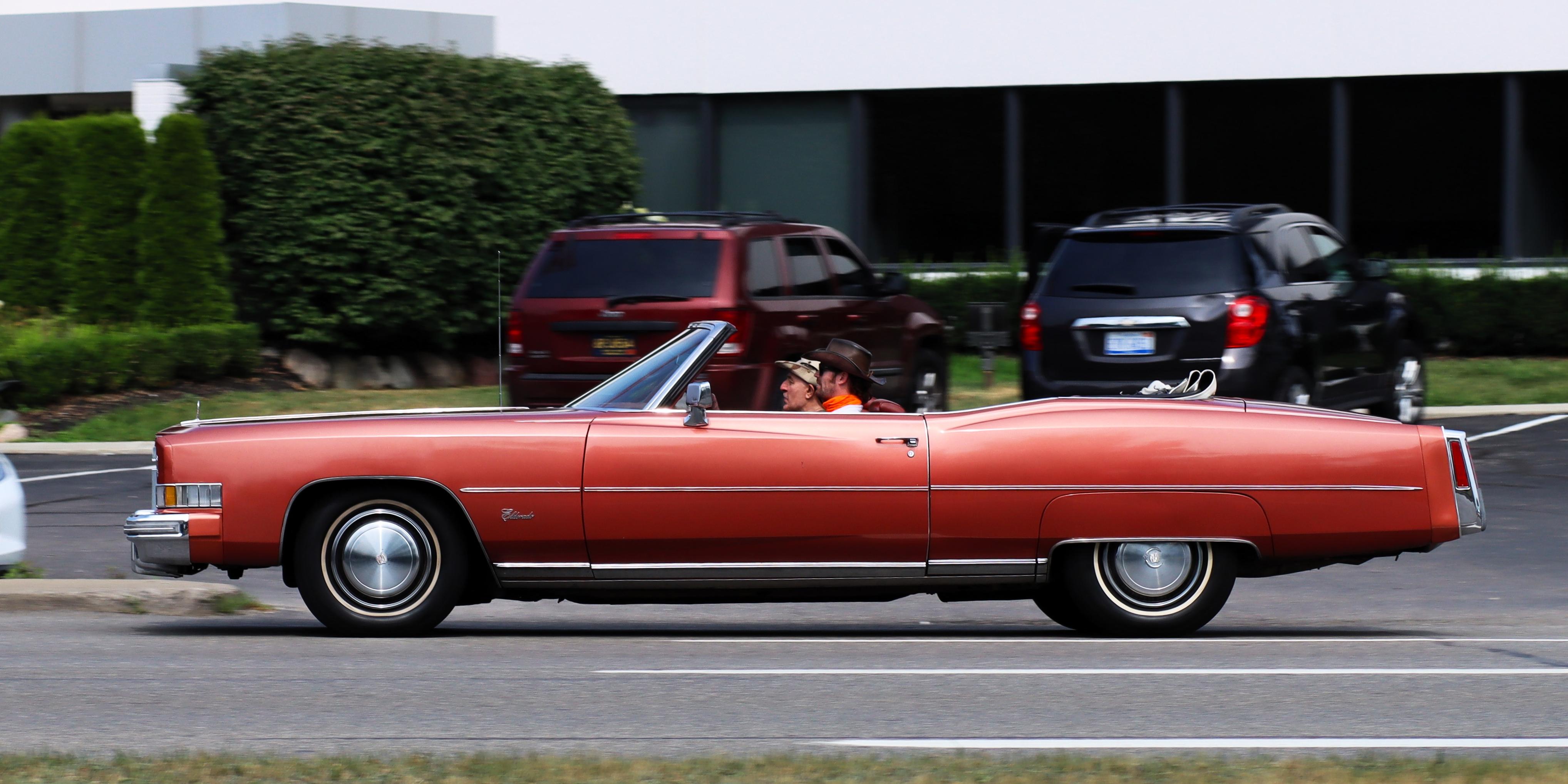 Photograph of a reddish orange mid-70s Cadillac Eldorado convertible seen from the left side.