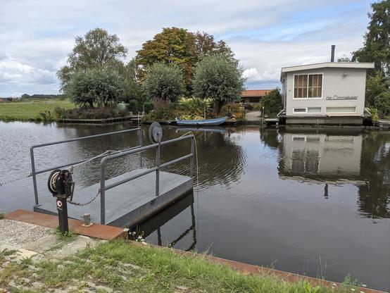 Along a calm canal, a small floating platform waits to act as a hand-powered ferry to reach a little house on the far side