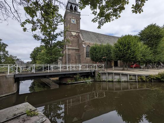 A brick church with clock tower stand by a bridge over a canal