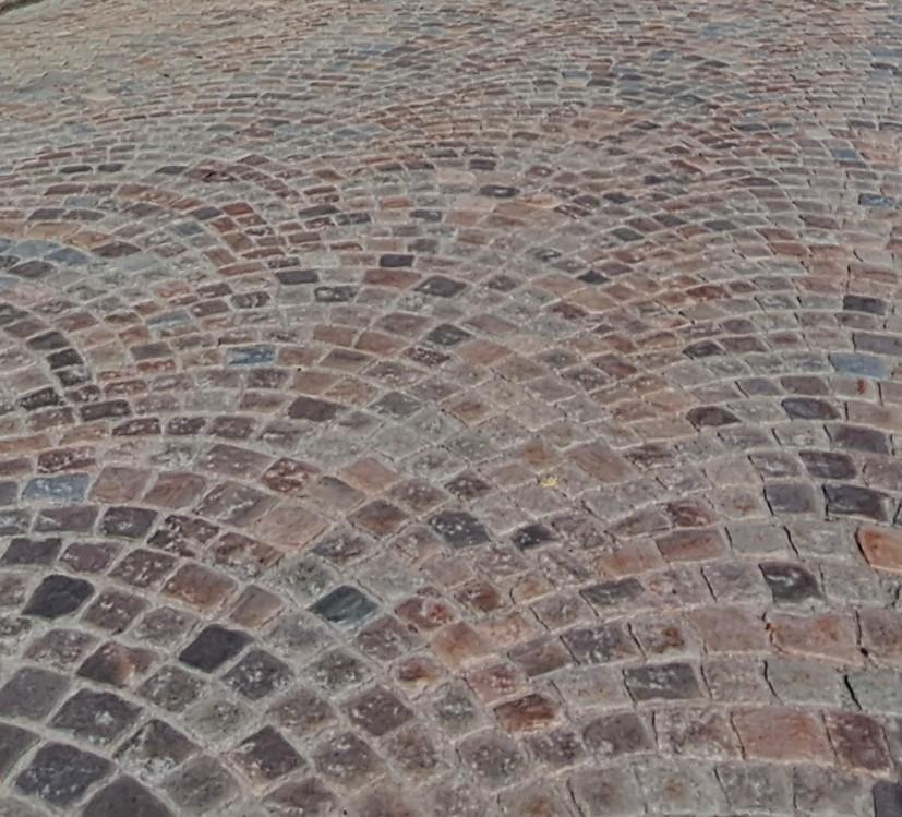 Das Foto zeigt den Blick schräg hinab auf eine mit Kopfsteinpflaster befestigte Straße. Die rötlichen Granitsteine sind in Bogenform verlegt.