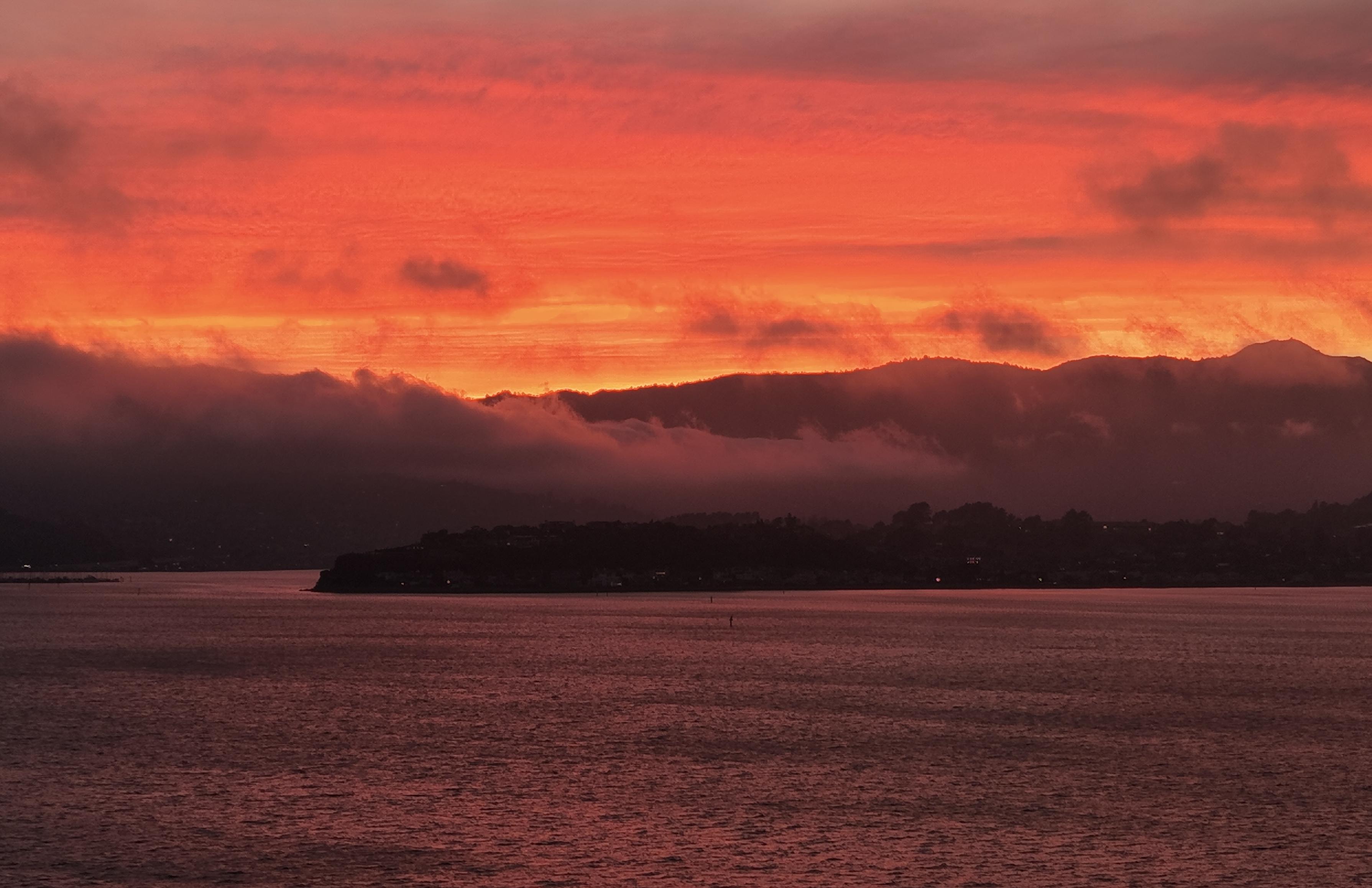 Photograph of sunset over Strawberry Point peninsula and the Marin Hills, taken from Richardson Bay
The sky is a dramatic yellow over the skyline banding to deep orange higher up.