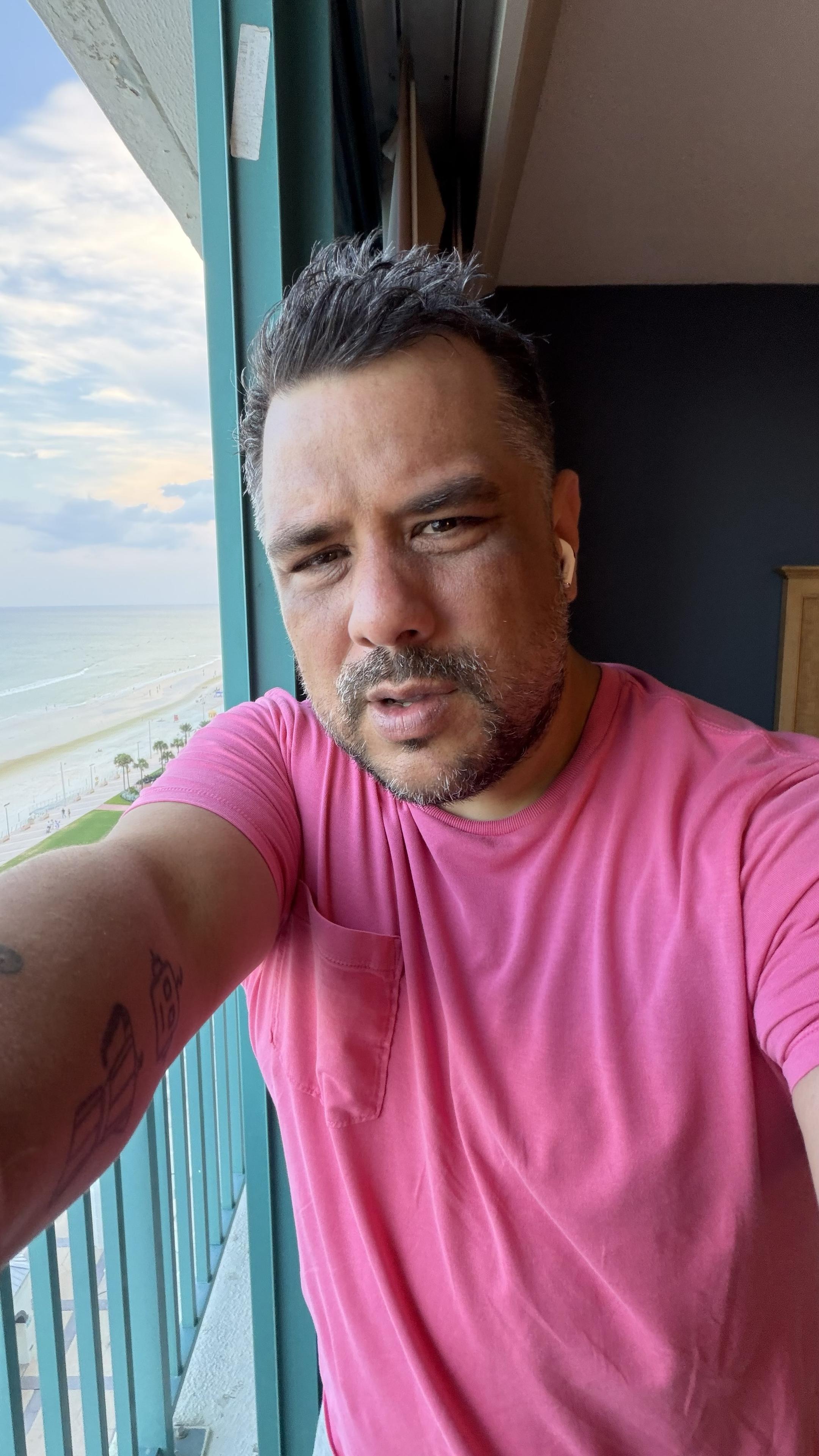 Photo of me standing on a balcony. There is the ocean and the beach. That contrasts my bright shirt.