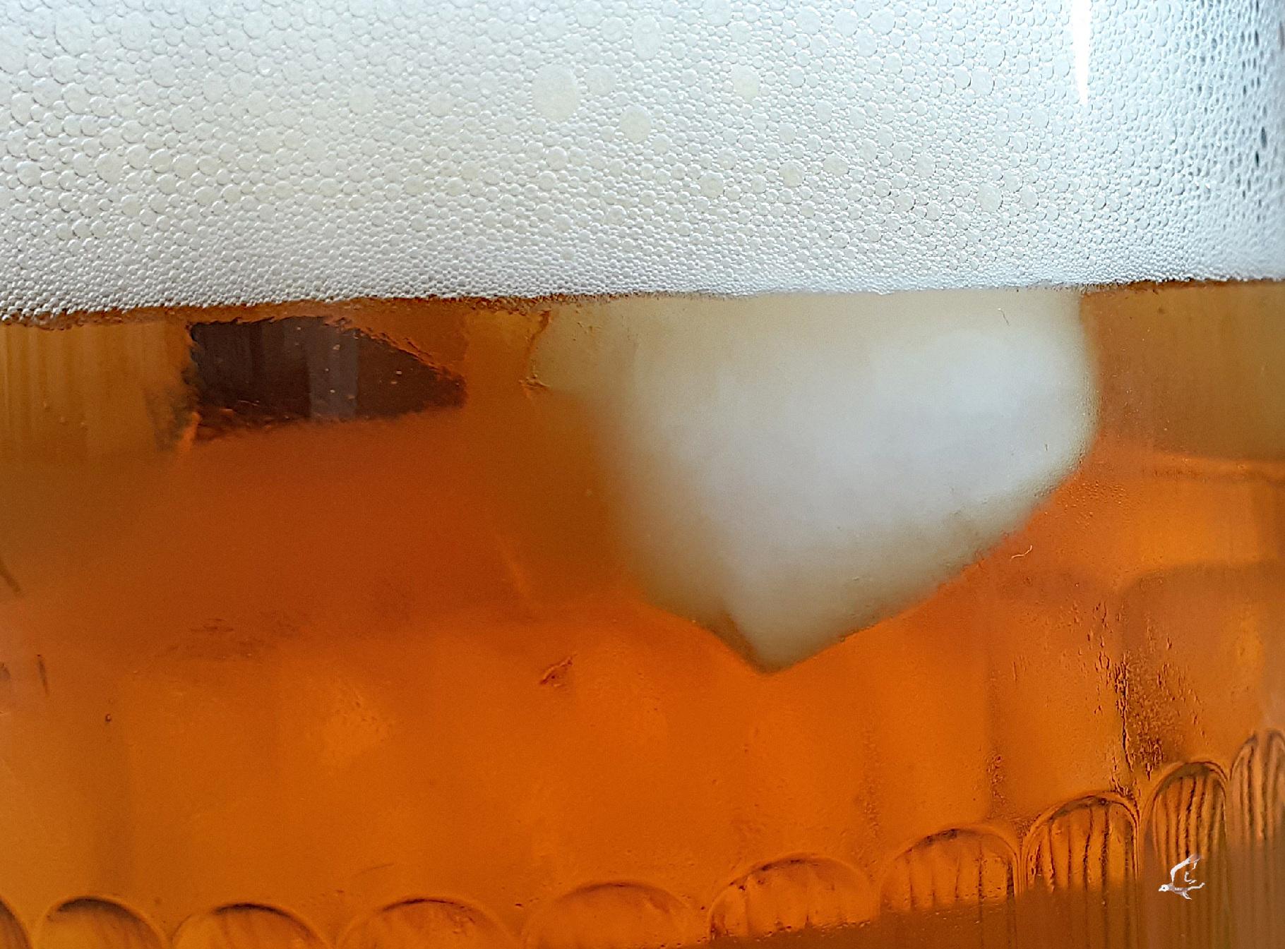 Closeup on a beer-glass with ice-cube and foam