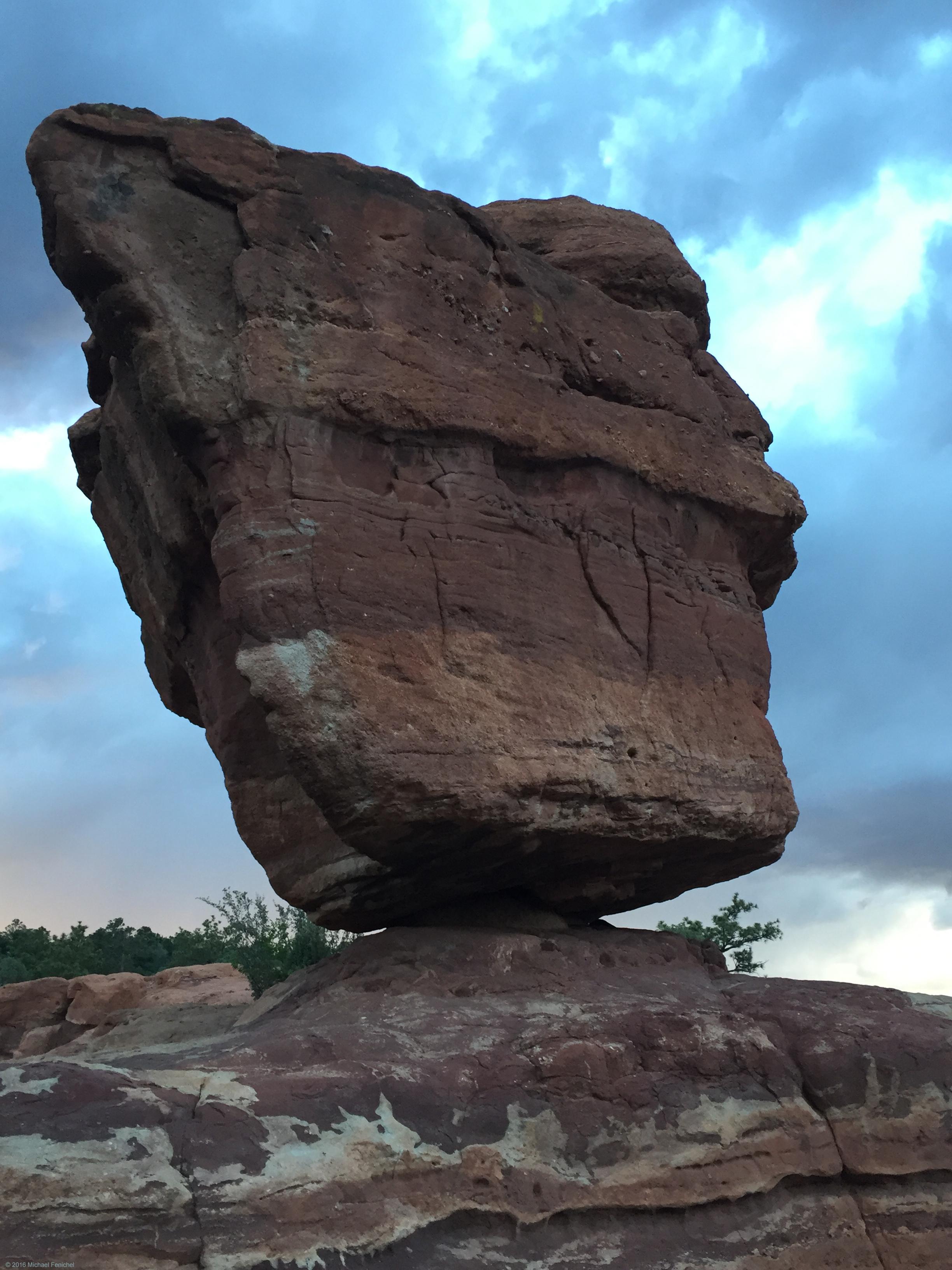 Photo by Fenichel - "Balance"

A huge reddish rock, about 3-4 'stories' tall, stands with its base very narrow, so thin it is like a spinning top which is precariously balanced. Below, the 'base' is red and white striated rock. Above and aorund the main rock formation, there is a blue sky mixed with white clouds.