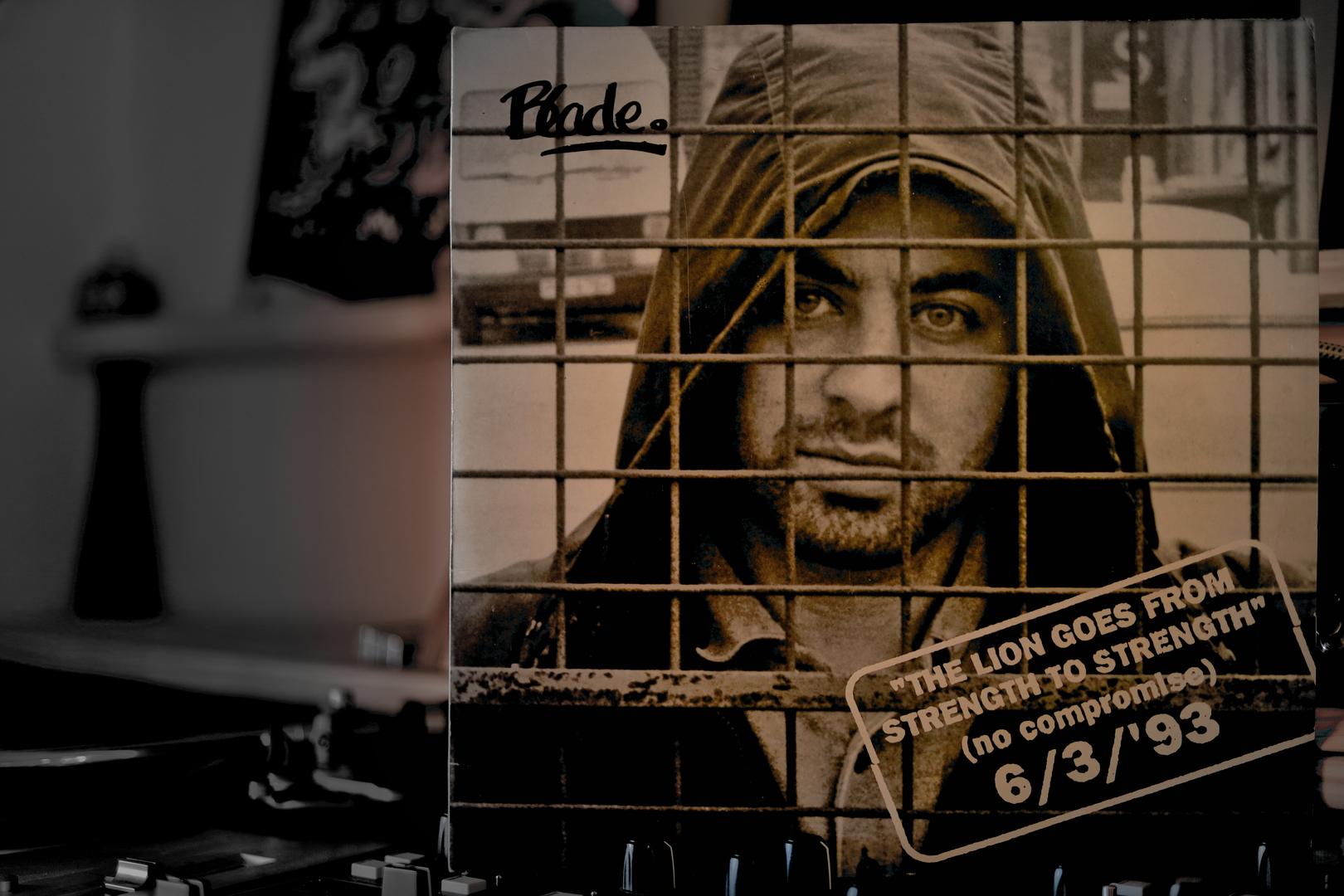 The Blade cover from the album “The Lion Goes From Strength To Strength” is on a mixer on the right side of the picture and takes up two-thirds of the frame. To its left, a turntable is blurred in the lower part of the frame, and above it is an out-of-focus background. The cover is clearly in the foreground.