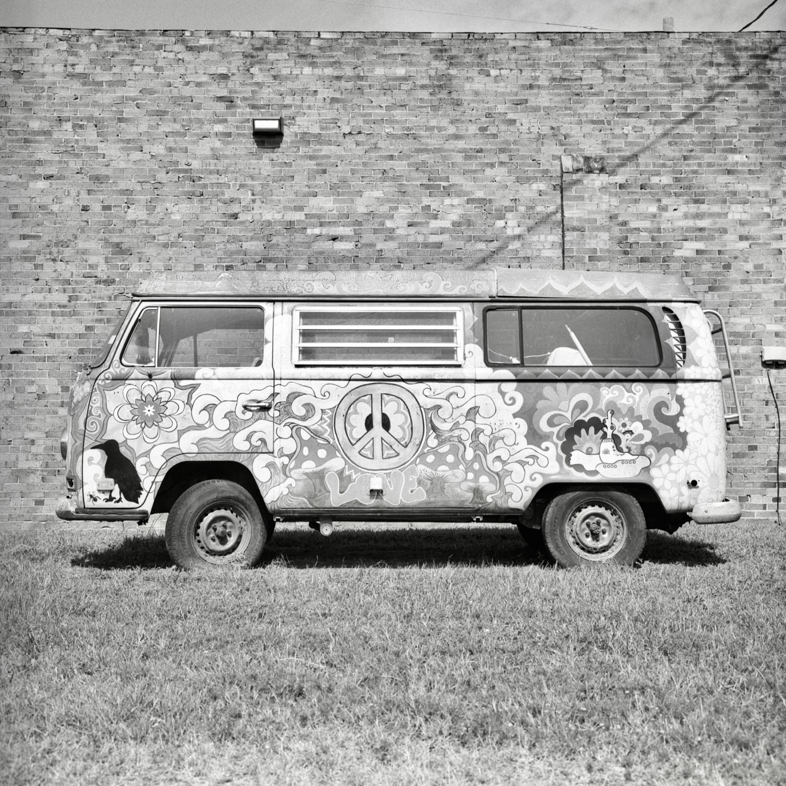 A black-and-white film photo. An old Volkswagen van is covered with psychedelic artwork, including a giant peace sign and the word “LOVE”, in Jefferson, Texas. Sunday, July 12, 2026.