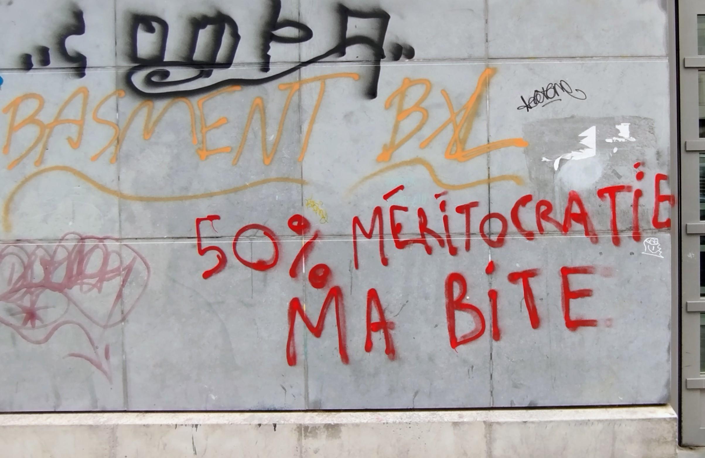 Photo couleur de rue.
Sur un mur gris, l'inscription en rouge :"50% méritocratie ma bite"