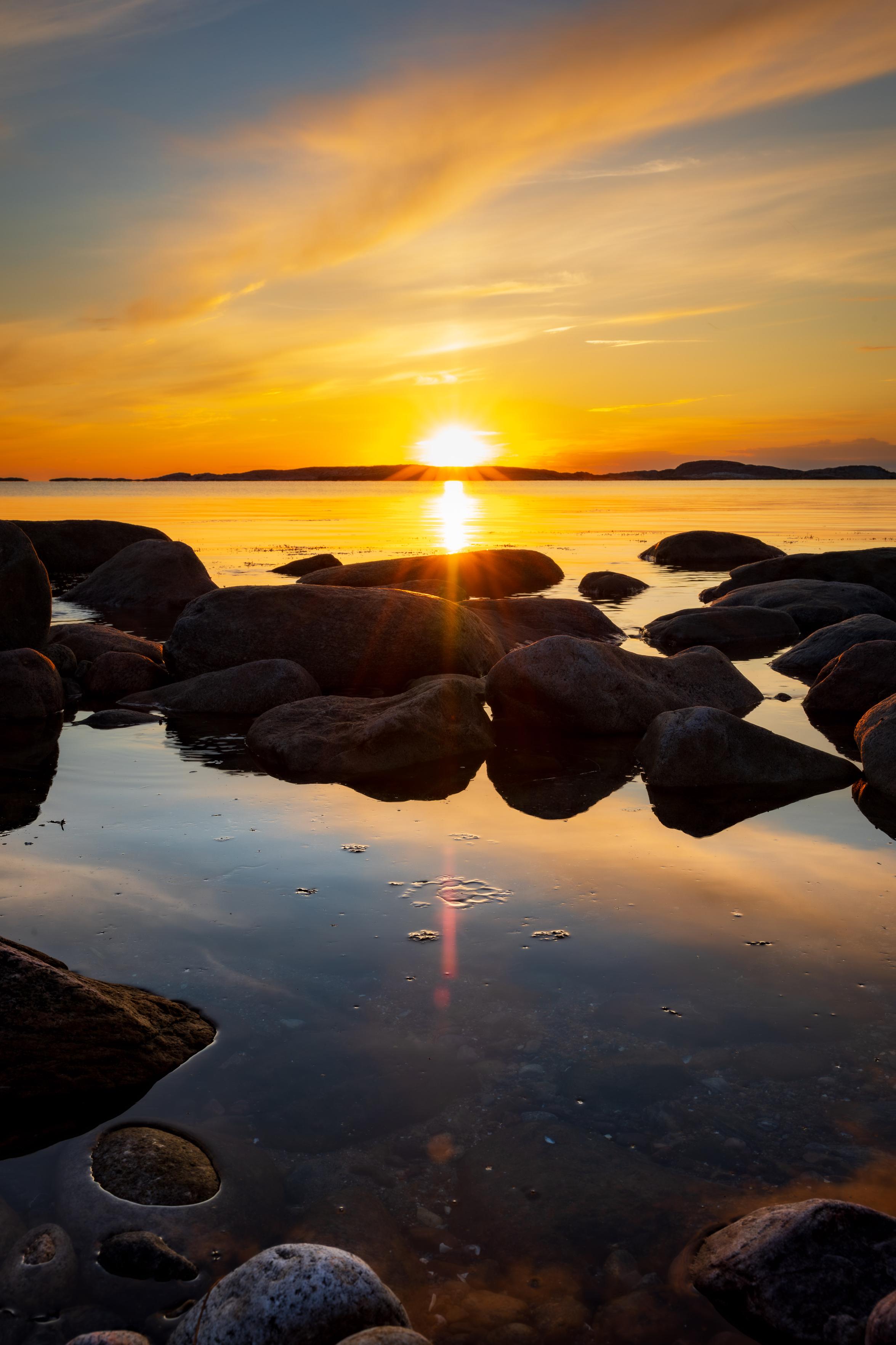 Sunset over the ocean with a small pond and rocks in middleground.