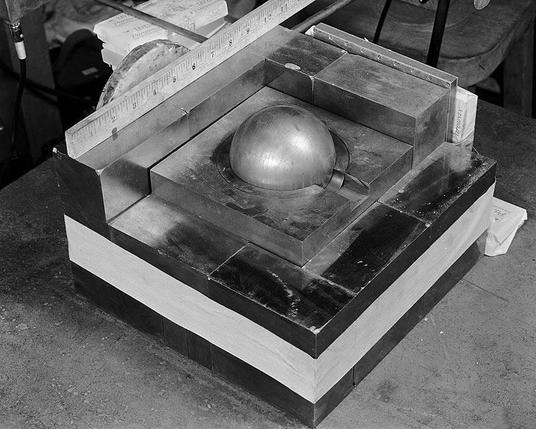 Eine Kugel aus Plutonium, umgeben von neutronenreflektierenden Blöcken aus Wolframkarbid. Eine Nachbildung des Kritikalitätsunfalls vom 21. August 1945 in Los Alamos, um die Strahlung zu messen, die entsteht, wenn ein zusätzlicher Block hinzugefügt wird, wodurch die Masse überkritisch wird.
Quelle: Los Alamos National Laboratory, From LANL's report on criticality accidents, 2000, http://www.csirc.net/docs/reports/la-13638.pdf PDF at http://www.csirc.net/library/la_13638.shtml