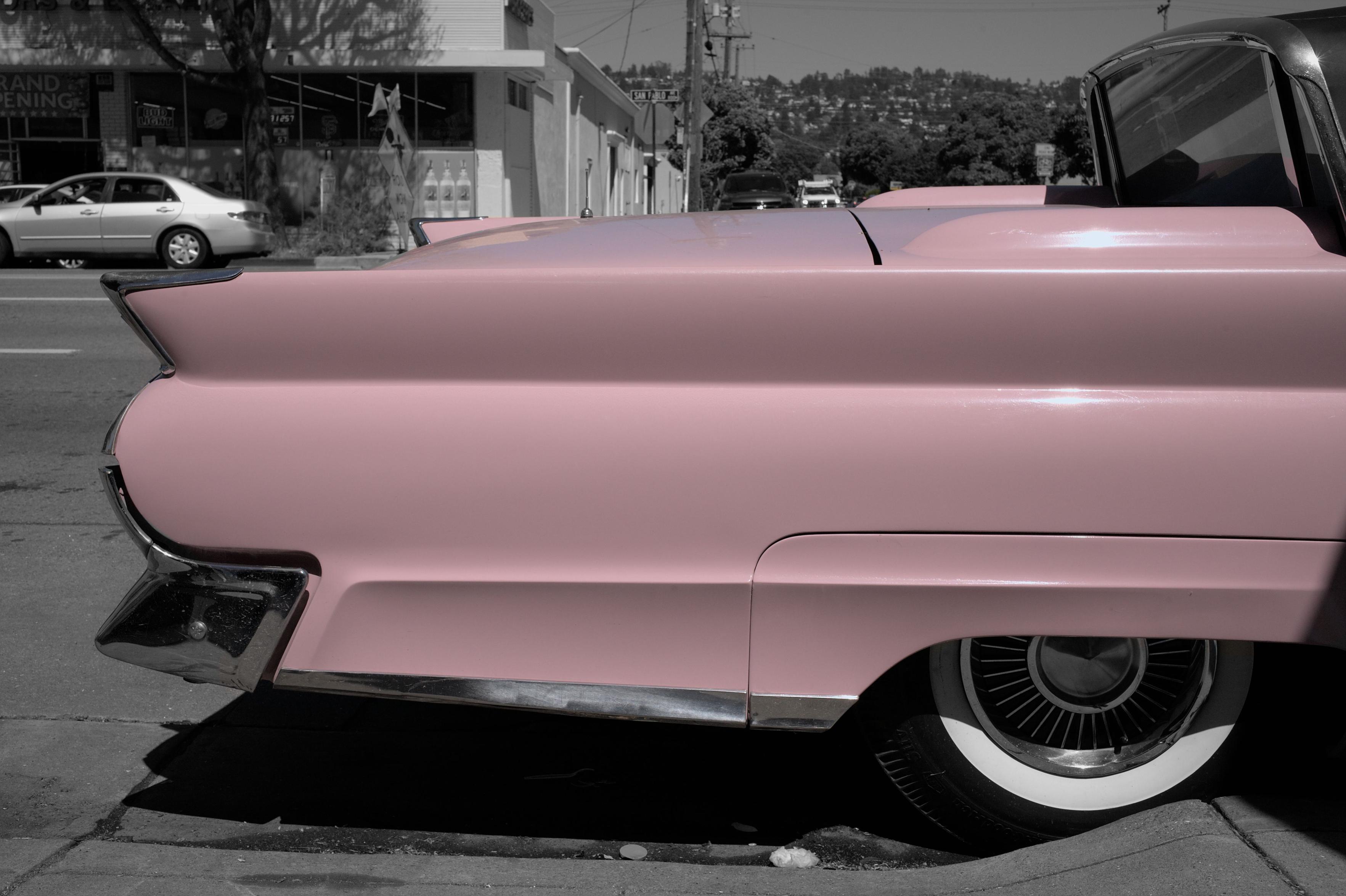 A black and white photo with the rear half of a parked old car painted pink.