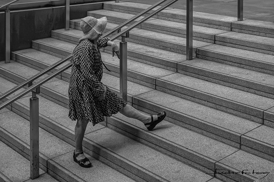 an old woman is climbing a stairway with her leg extended as if she was doing the goose-step.