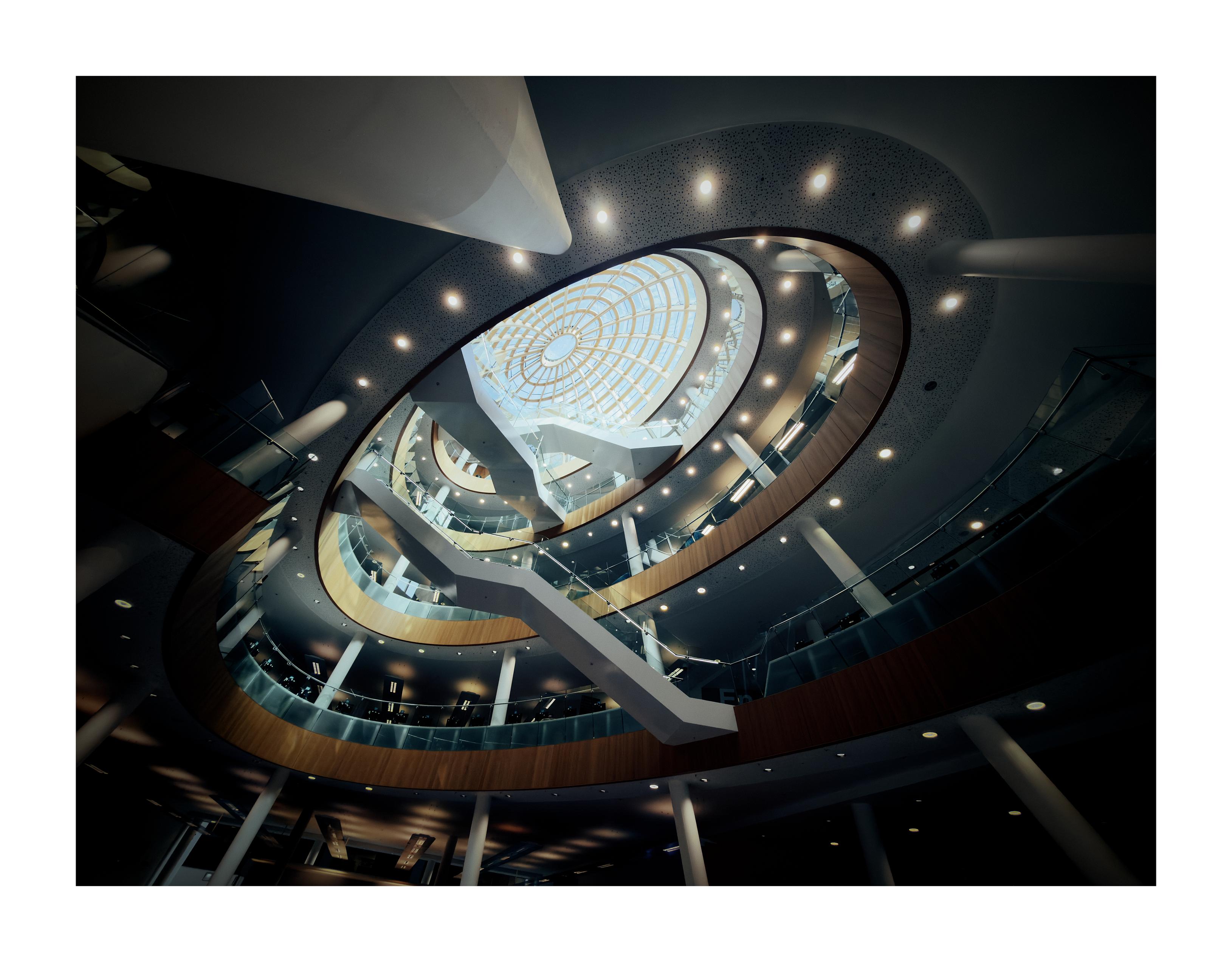 A futuristic interior of a library with stairs leading up towards a glass dome.