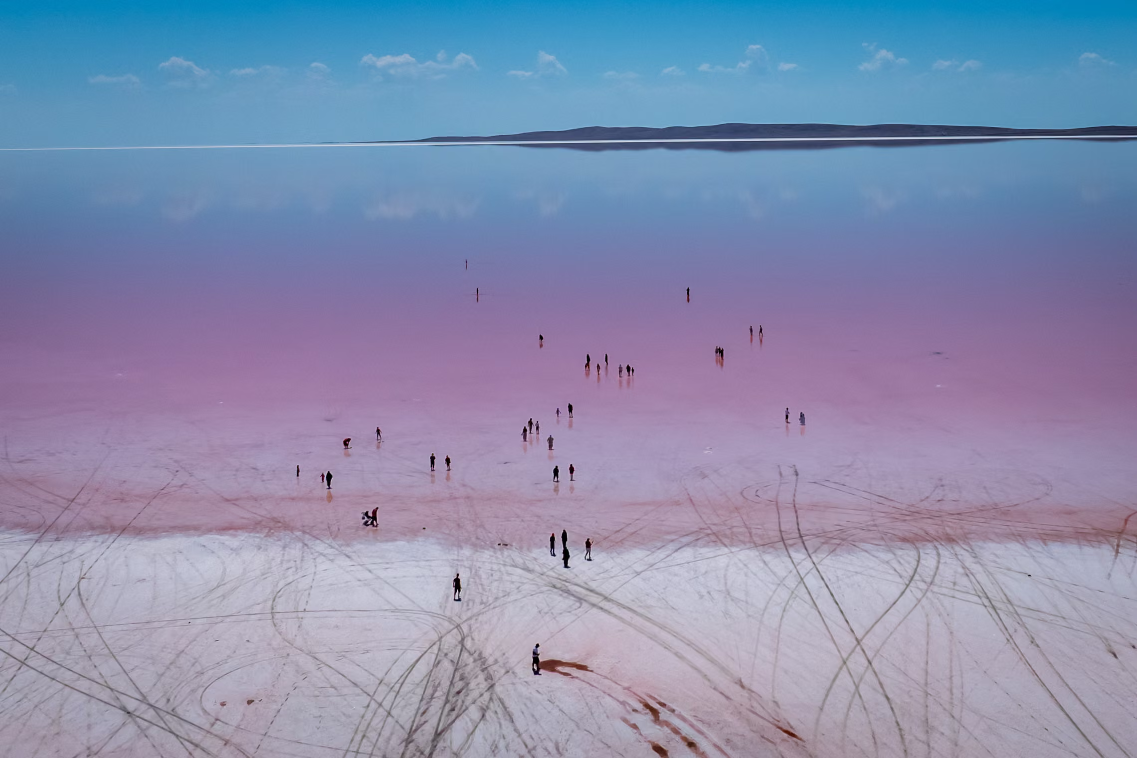 Visitors wade in the vibrant pink shallows.