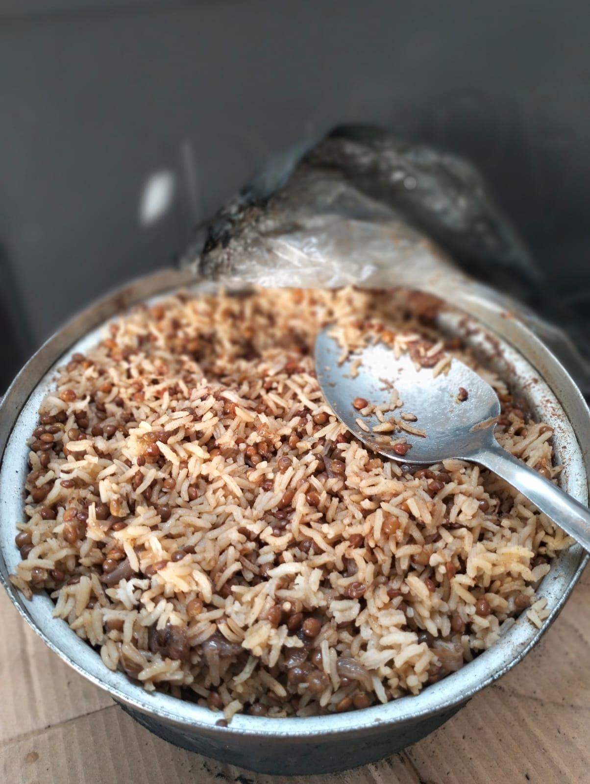 A metal bowl filled with rice and lentils, with a metal spoon resting on top of the food.