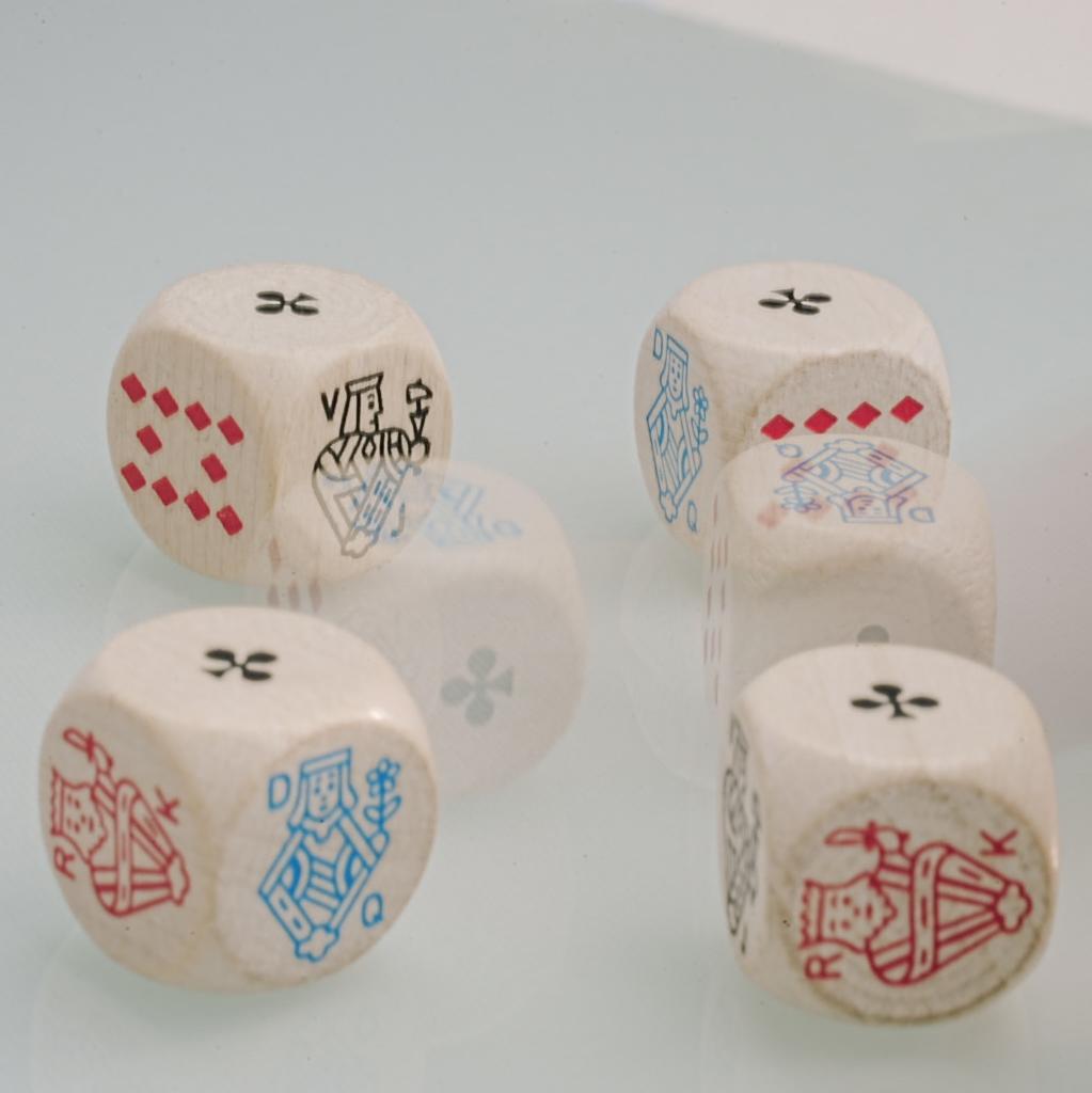 5 weiße Holzwürfel mit Symbolen aus Kartenspielen liegen auf einer hellen Oberfläche. Jeder Würfel ist an den Kanten leicht abgerundet. Sie zeigen verschiedene Symbole wie Karo, Kreuz, Pik, König und Dame in Rot, Blau und Schwarz. Die Würfel sind verstreut angeordnet, einer davon ist durch Bewegung verschwommen und 2x zu sehen.