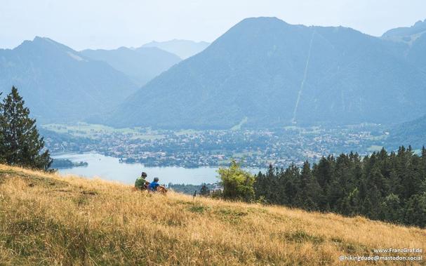 A view over a dry meadow down to a lake with mountains in the back