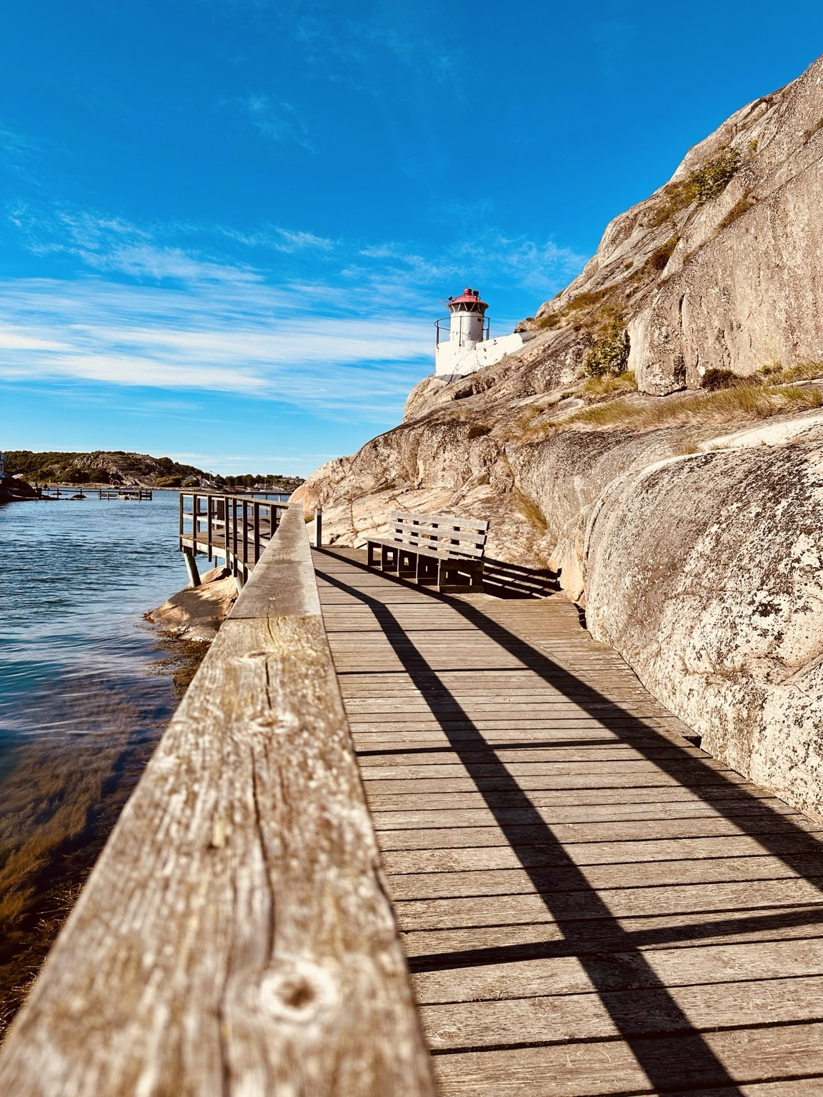 A wall bridge along a rock and a canal with a lighthouse top right.