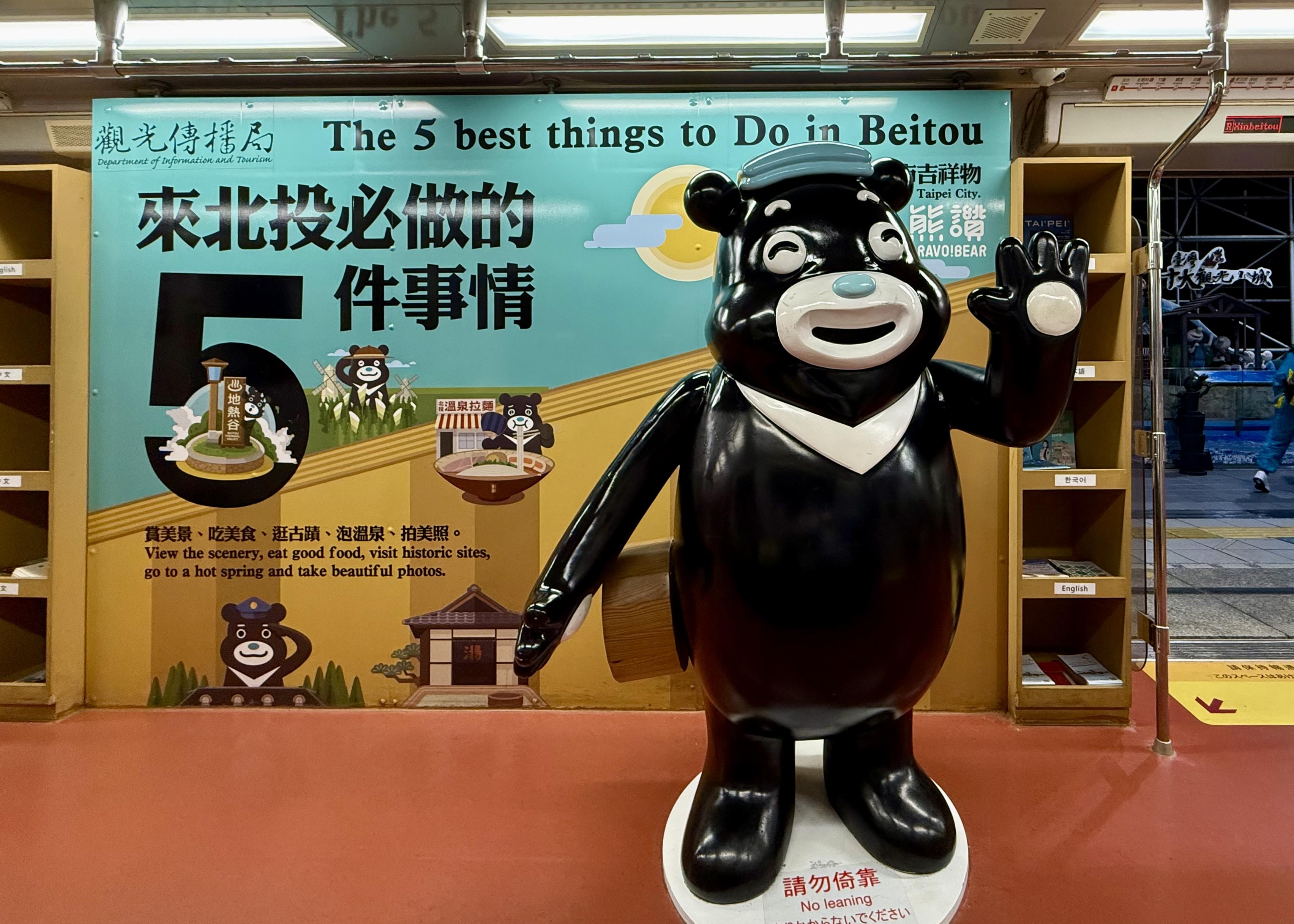 A life-sized black bear statue with a white face, waving and smiling, stands in front of a colorful sign promoting top activities in Beirut.
