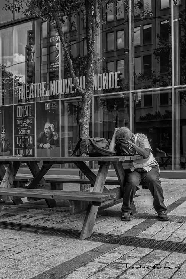 A woman is asleep in front of a theater, Holding her head the same way a man is holding his head on a poster in the front window.