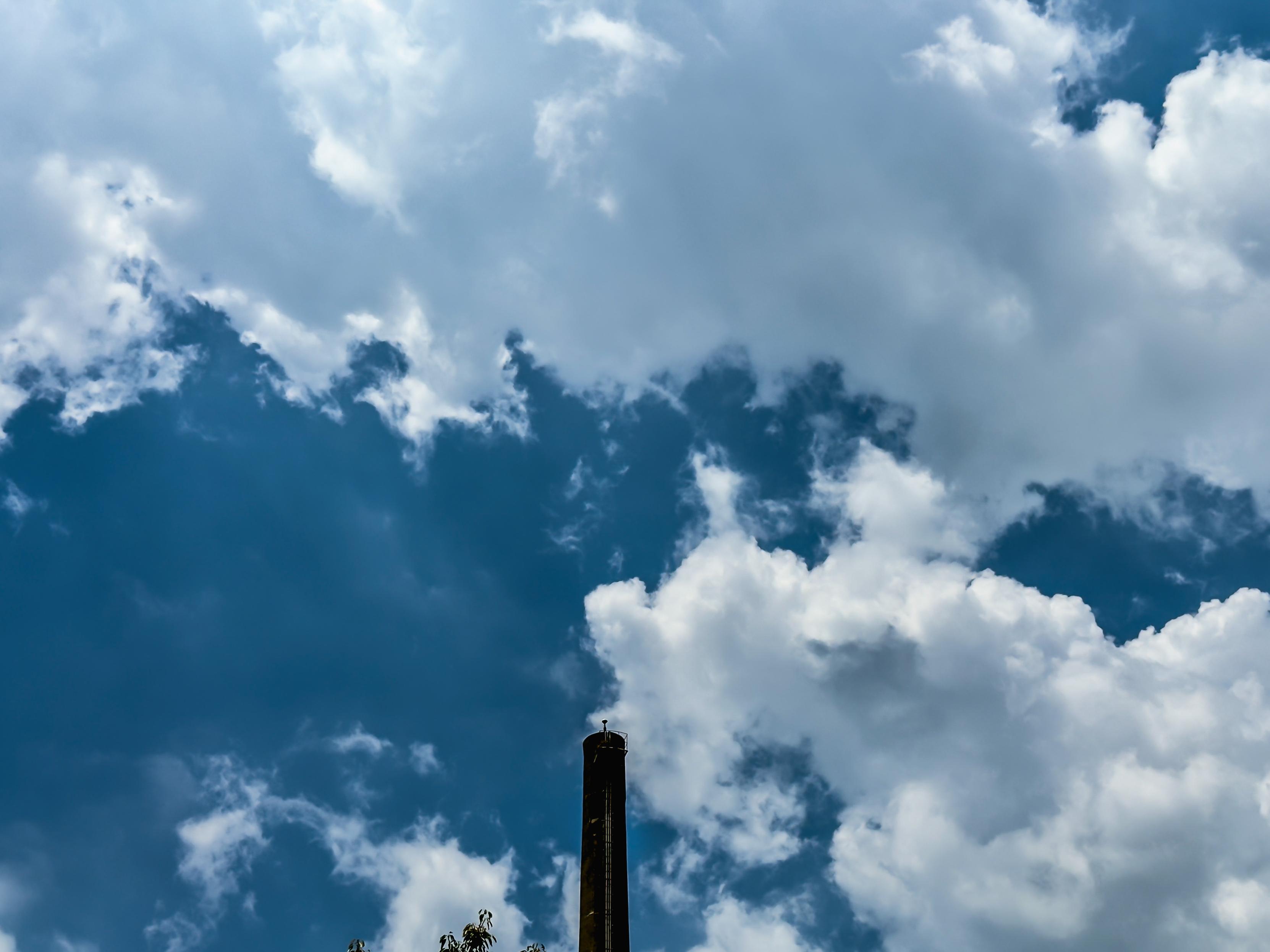 A tall chimney or smokestack reaching up towards a partly cloudy sky with white and gray clouds.