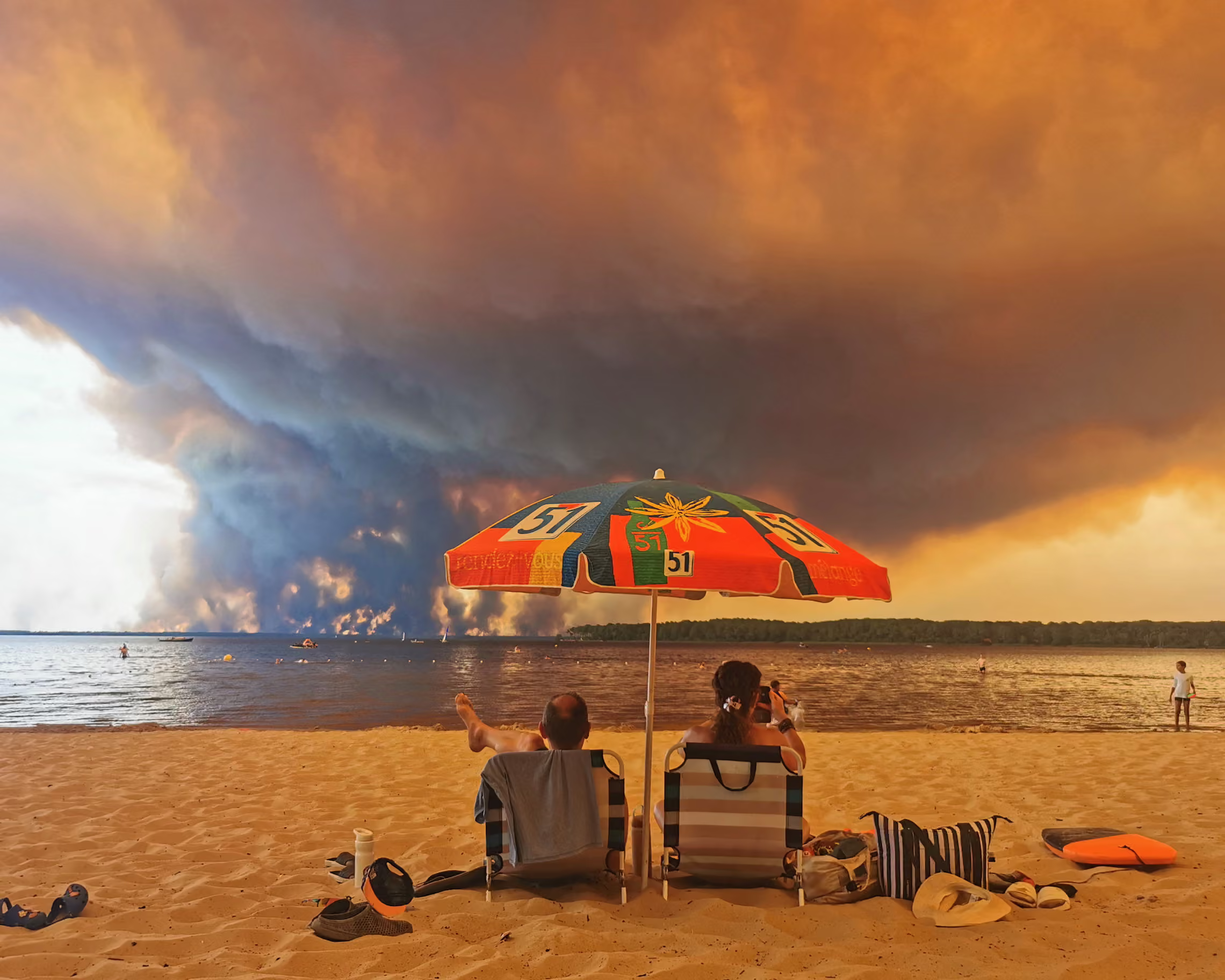 A couple on a beach, watching apocalyptic fire on the other side of the lake.